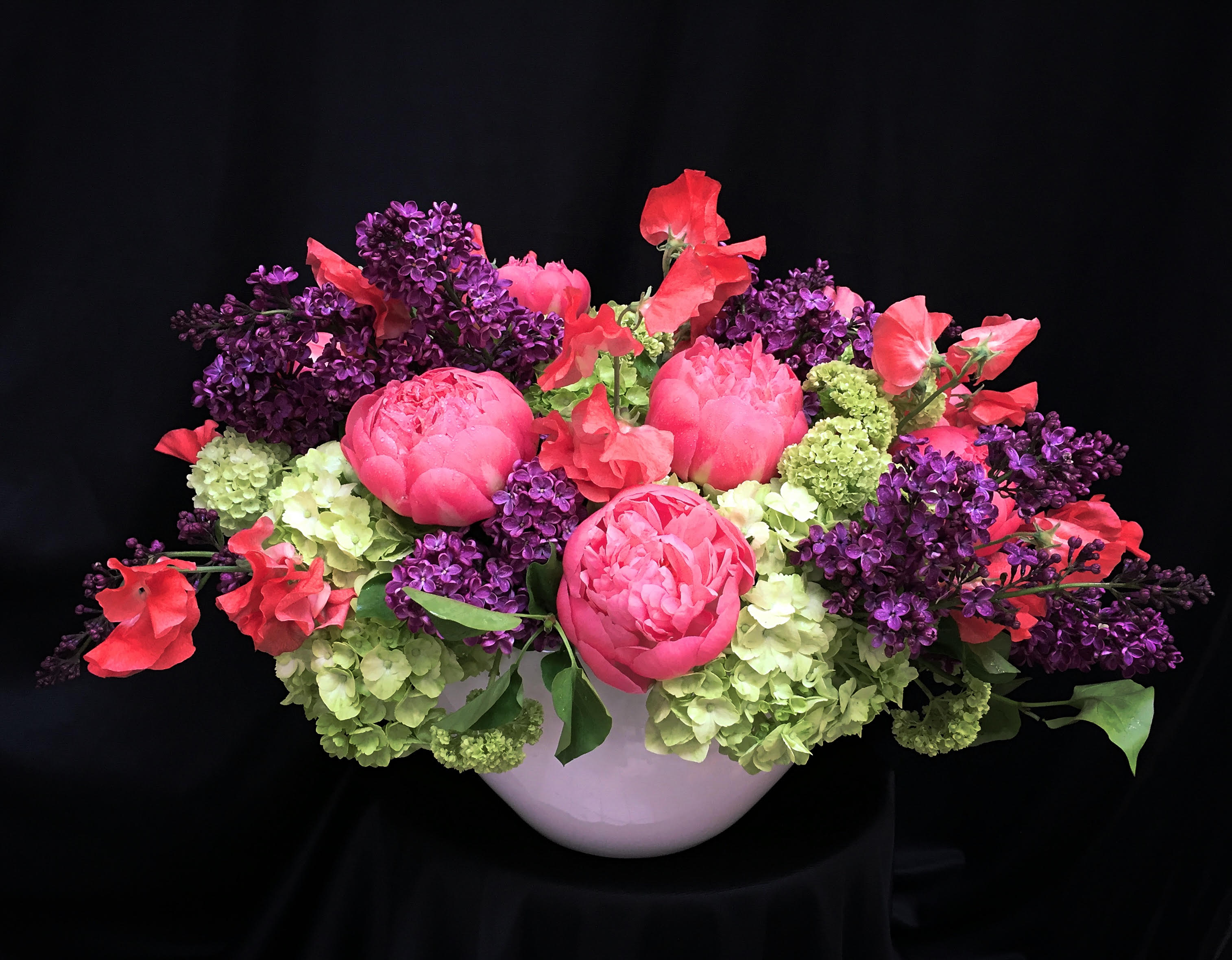 Pink peonies and purple lilacs arranged in a white bowl vase