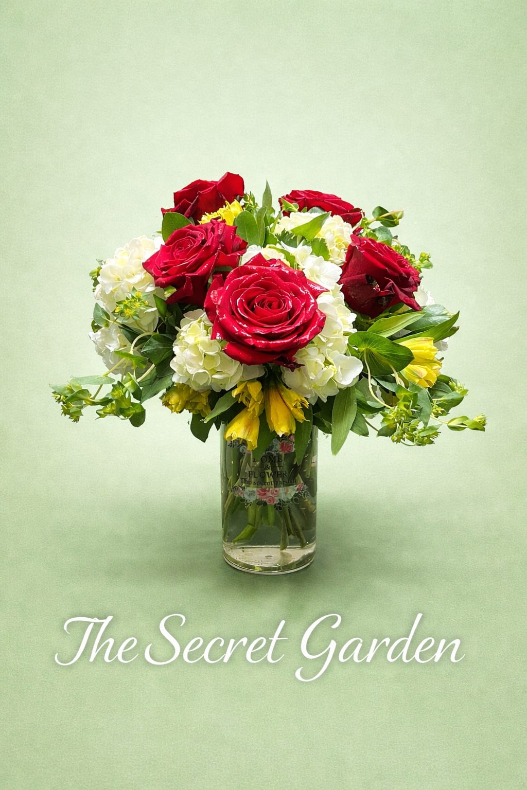 The Secret Garden Bouquet - A cluster of rich red roses arranged above a cloud of white hydrangea-like blooms creates an instant romantic statement-perfect as an anniversary bouquet or a birthday surprise for the person you love.   The design pairs large red roses with white hydrangea-style flowers, yellow alstroemeria accents, and lush green foliage in a clear glass vase for a full, rounded look. A pale pink ribbon bow ties to the front for a soft contrast and feminine touch; the compact, upright presentation is formal enough for an anniversary yet warm and celebratory for birthdays or thank-you occasions. Available with the balloon option and finished in a glass vase, this arrangement arrives ready to display and delight.  Choose Secret Garden when you want her to feel truly seen-romantic, cherished, and celebrated. Vase dimensions and exact bow color may vary; simple care (fresh water and a sunny spot out of direct heat) helps blooms stay lovely through the special week after delivery.