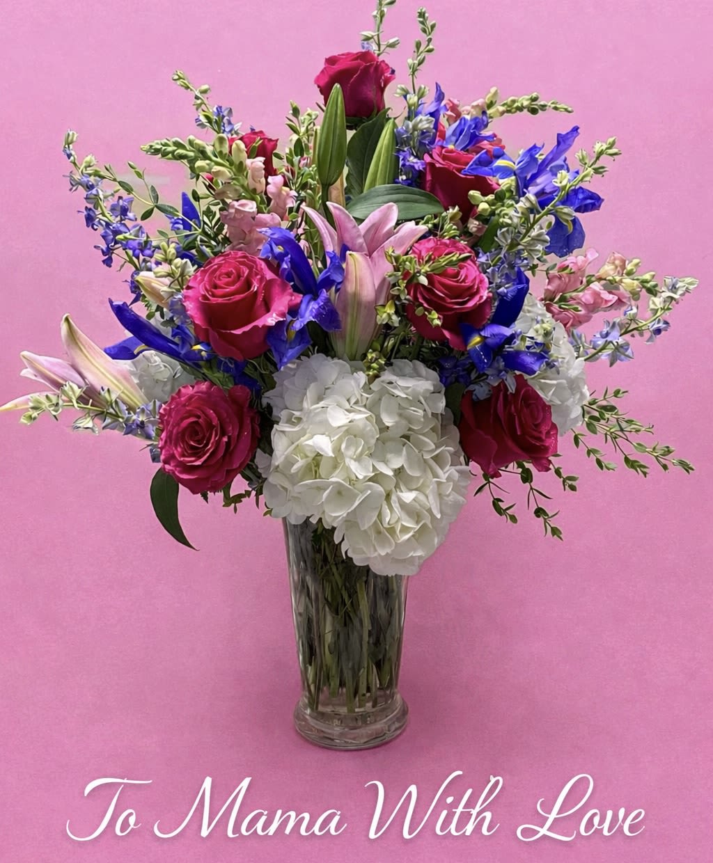 To Mama With Love Bouquet - Soft, uplifting and classically elegant, this flower arrangement - the perfect Mother's Day bouquet - blends white roses, daisy-like blooms, carnations and lilies with pops of pale blue, pink and purple to create a gentle, comforting presence. The mix reads as both serene and celebratory, so it also makes a thoughtful sympathy tribute, a graceful thank-you, or a "thinking of you" gift for birthdays, anniversaries, get well wishes, or just because moments.  Built full and rounded, the bouquet mixes textures: creamy white hydrangea clusters and roses sit alongside layered carnations and alstroemeria, while snapdragons and small blue accent flowers add height and a cool, airy contrast against glossy green foliage. Stems are arranged in a clear glass vase so the natural lines and water show through, offering a classic florist presentation that suits housewarming, retirement, graduation, or holiday tables. Order sizes accommodate different gestures - from intimate bedside cheer to a more generous centerpiece - and simple care (fresh water and a cool spot away from direct sun) keeps the blooms looking loved for as long as possible.