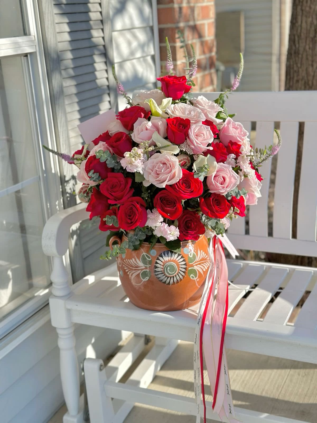 Abrazo de Amor Maternal( ollita tradicional ) - Honra a mamá con este elegante arreglo, donde las rosas rojas y rosadas se entrelazan en perfecta armonía.entre detalles verdes con aroma a eucalipto,  Todo presentado en una encantadora ollita de barro pintada a mano, ideal para transmitir amor y gratitud en el Día de las Madres, disponible todos los días .