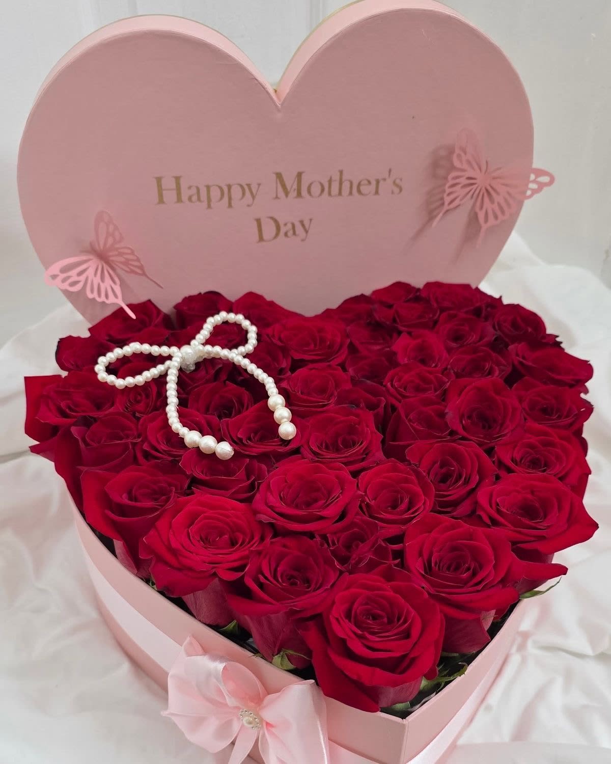 Timeless Love for Mom  - Surprise Mom with this elegant heart-shaped box, designed to make her day truly unforgettable. It features premium red roses, beautifully arranged for a luxurious and timeless look. The soft pink box, with “Happy Mother’s Day” lettering, is accented with delicate butterflies and a pearl bow at the center, finished with a satin ribbon for an extra touch of elegance.