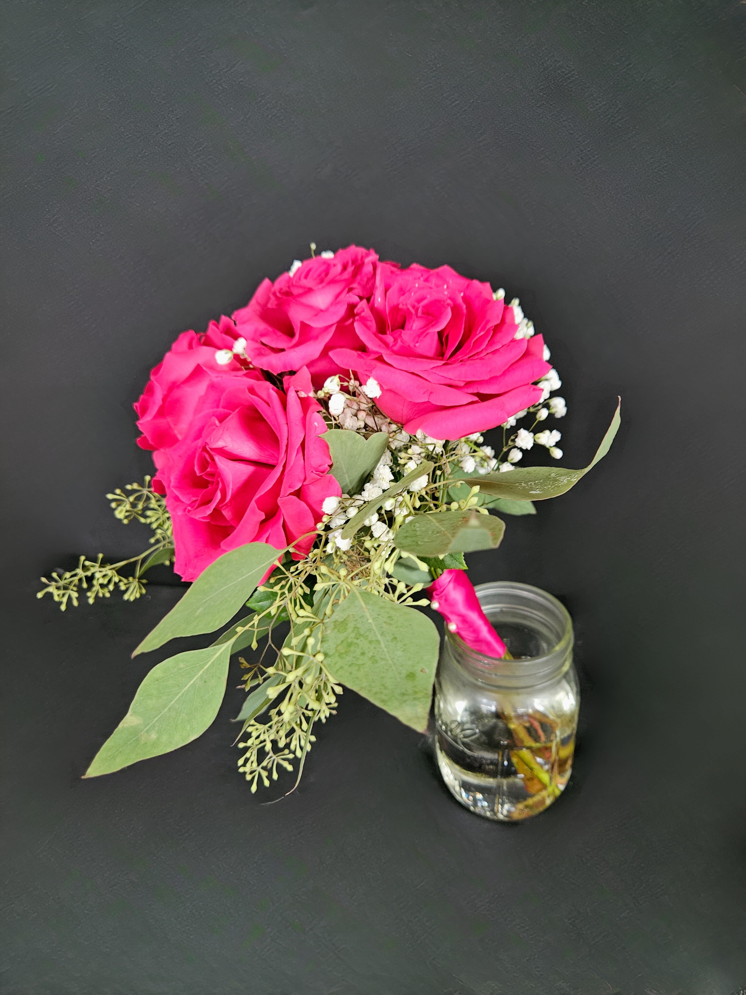 Pink roses with baby's breath and greenery beside a small glass jar