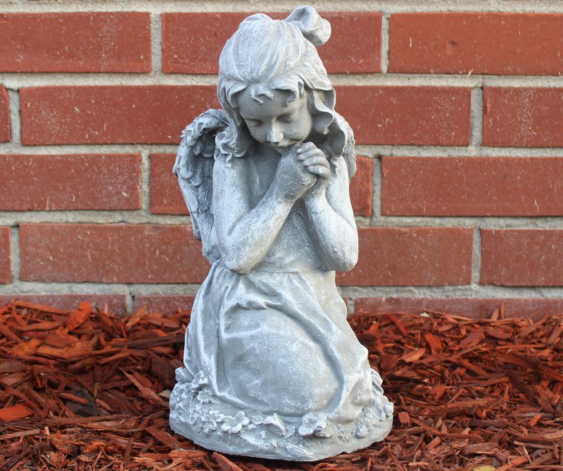 Gray praying angel statue in front of a brick wall