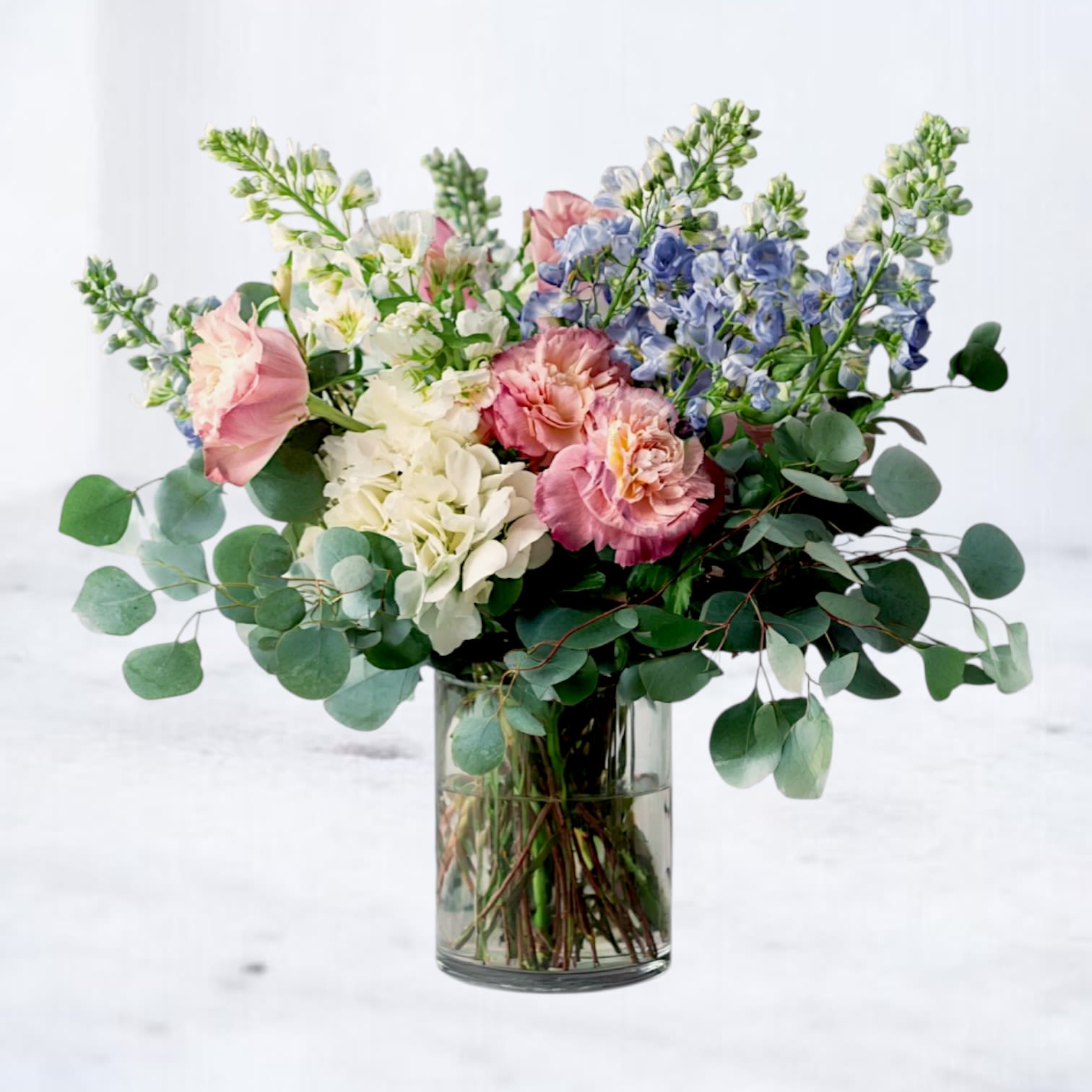 Bouquet of pink, white, and blue flowers in a clear glass vase