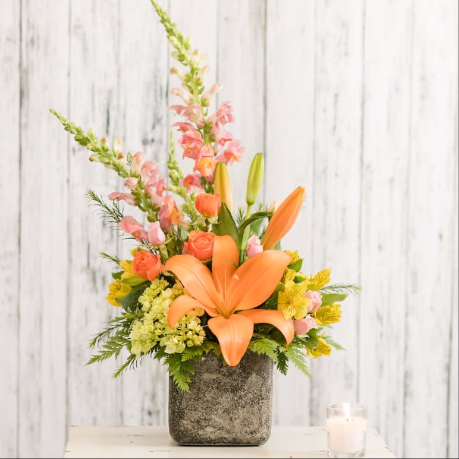 Orange lilies and pink flowers arranged in a gray vase