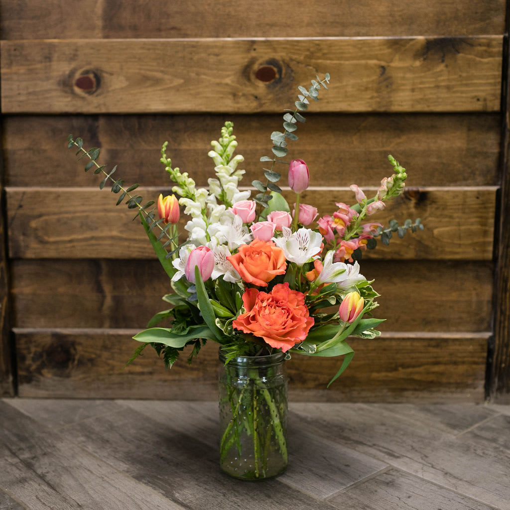 Mixed bouquet of pink, white, and orange flowers in a glass jar vase
