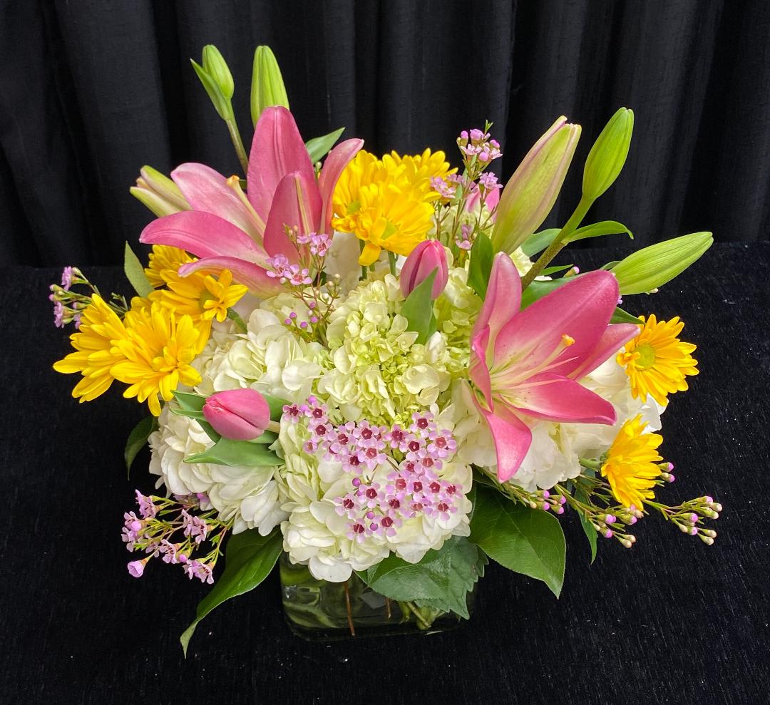Pink lilies and yellow daisies arranged with white hydrangeas in a glass vase