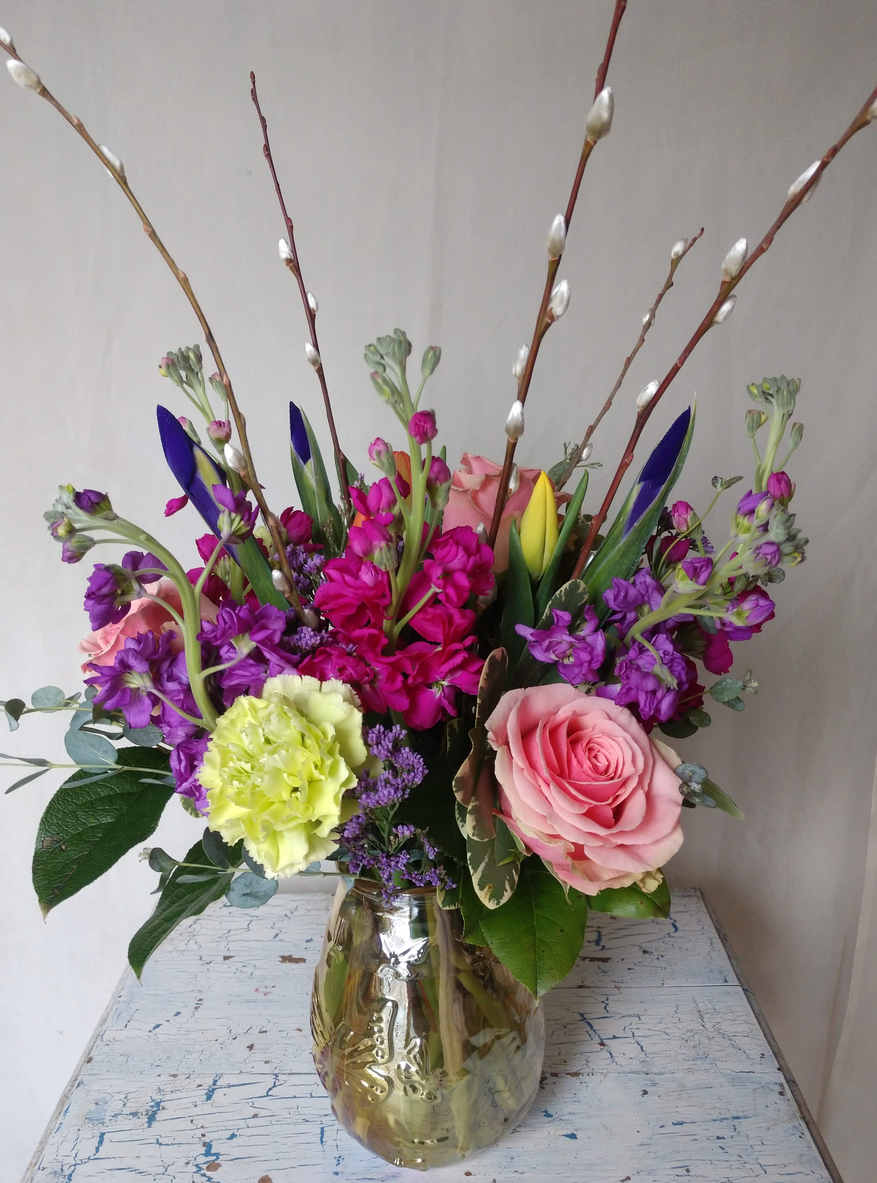 Mixed bouquet of pink roses, purple blooms, and pussy willow in a glass vase