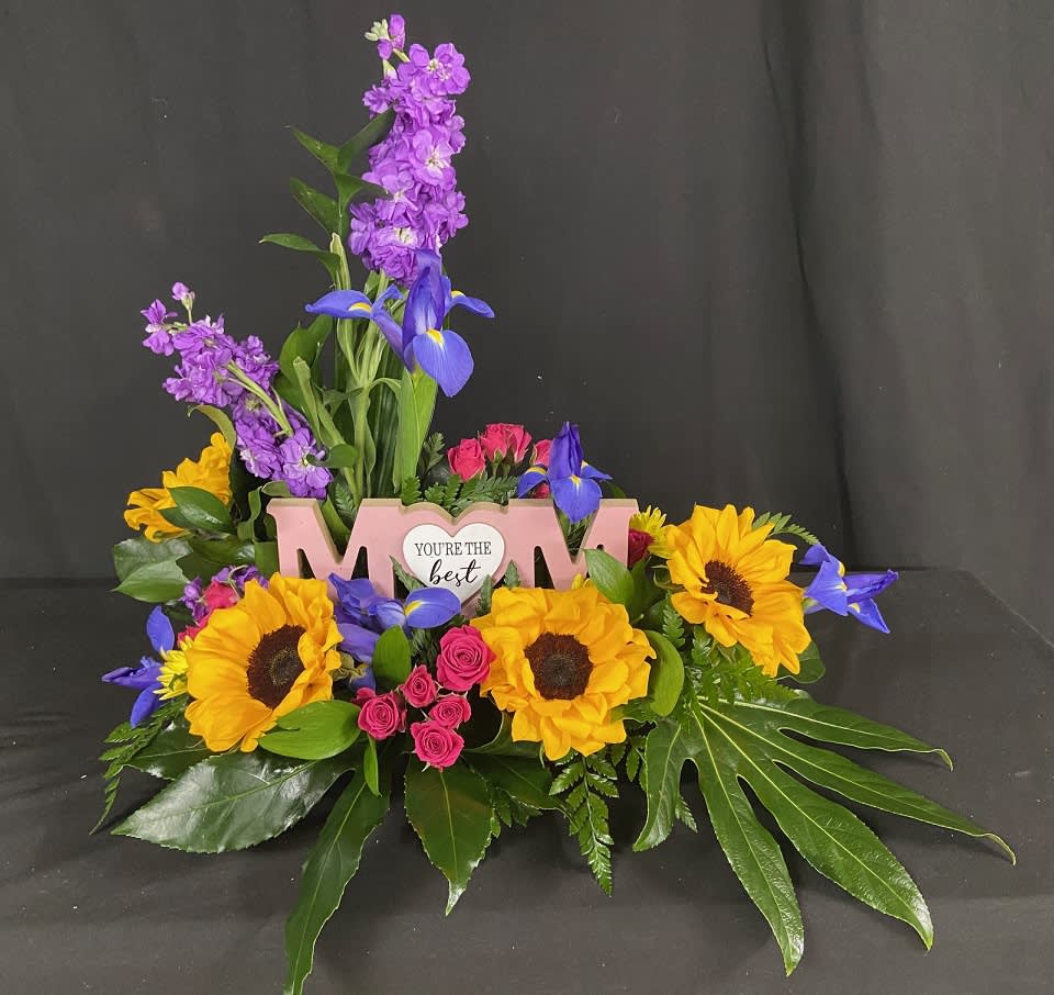 Colorful floral arrangement with sunflowers, purple blooms, and pink roses around a "Mom" sign