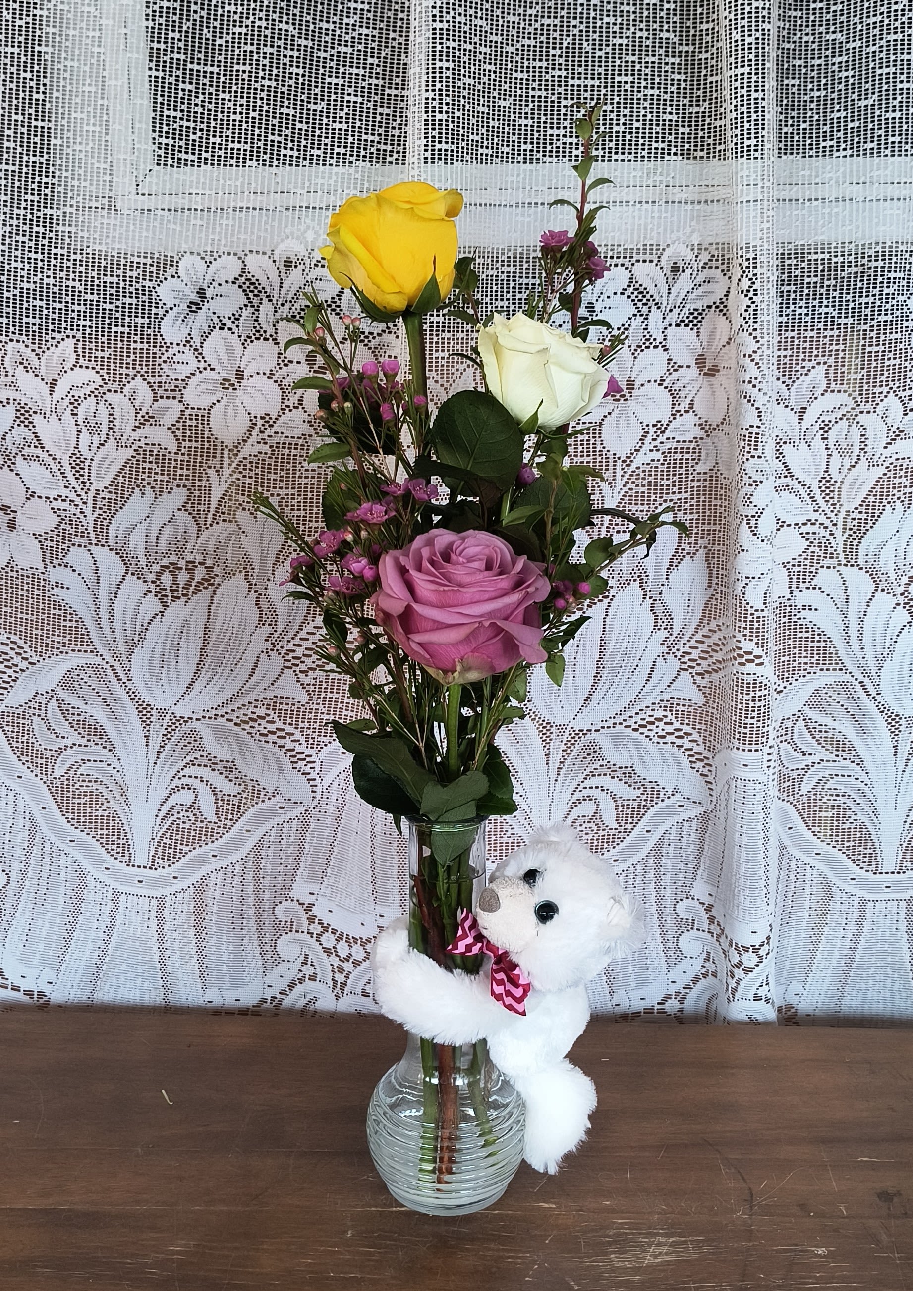 Mixed roses in a glass vase with a small white teddy bear