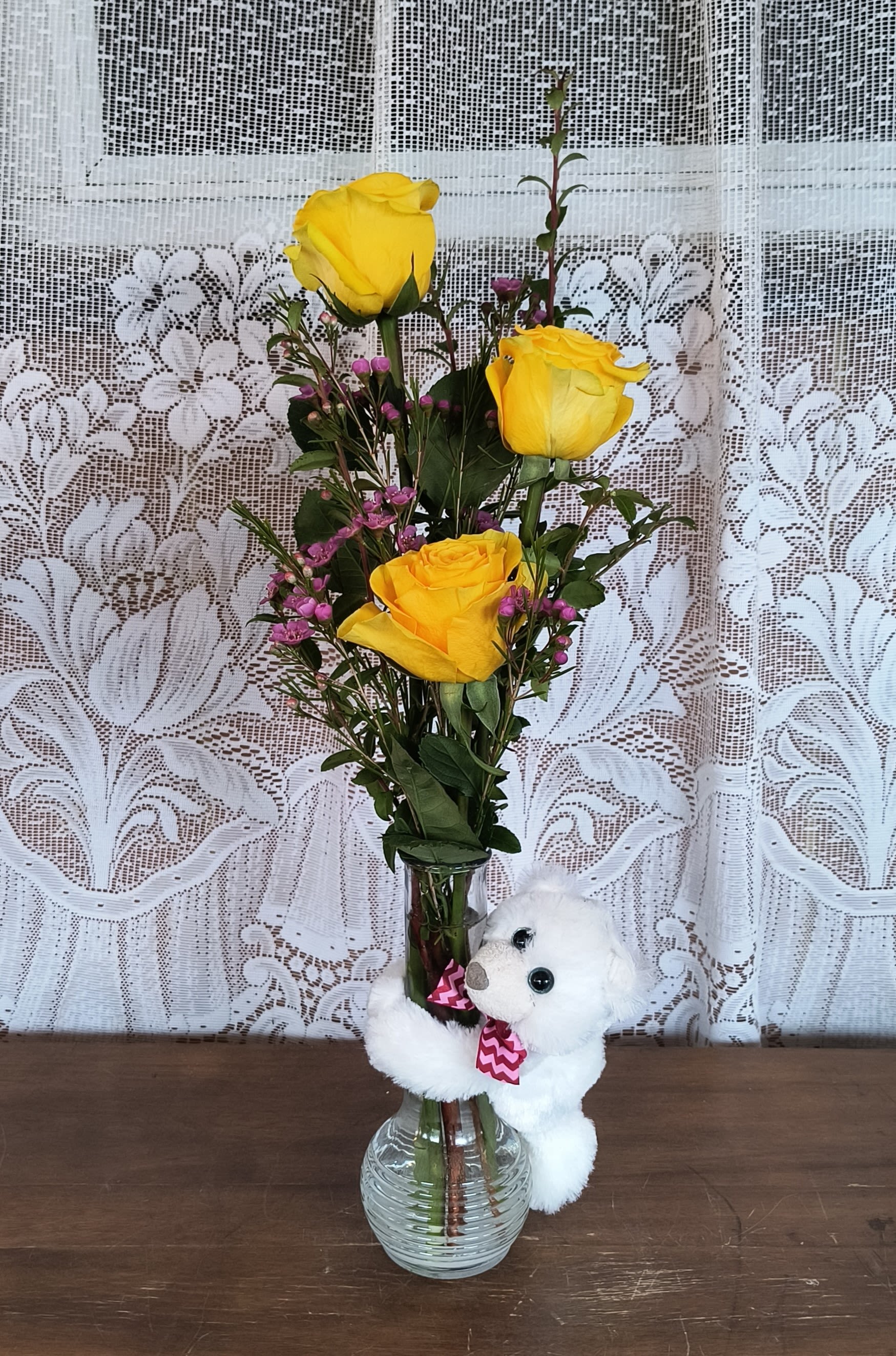 Yellow roses in a glass vase with a small white teddy bear