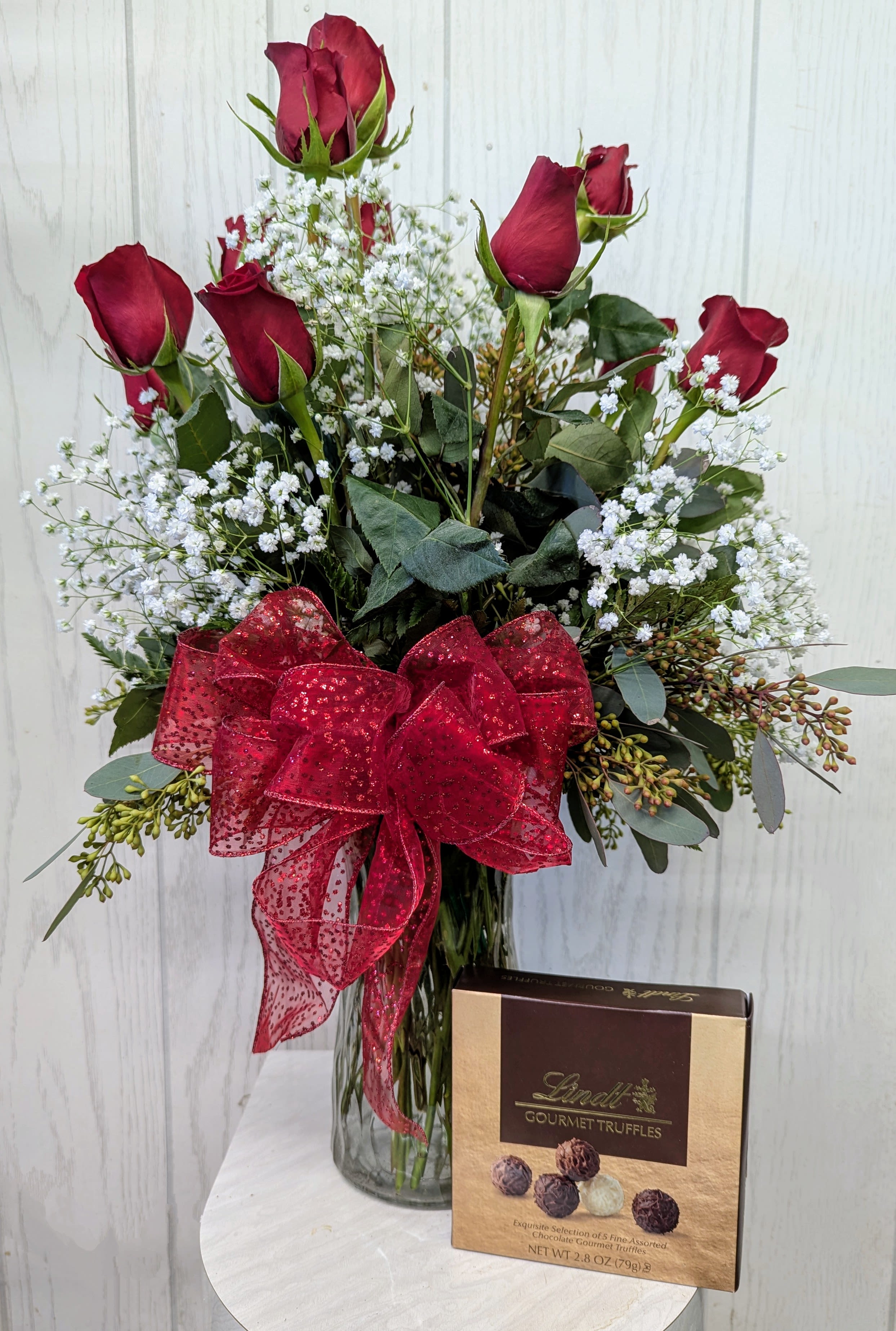 Red roses in a glass vase with a red bow and a box of truffles