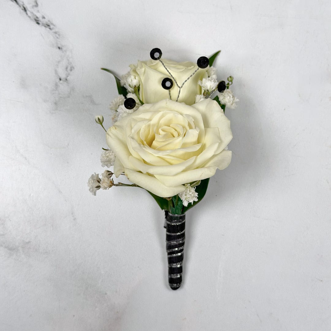 Onyx Boutonniere - With Wrap and Sparkle - Two ivory-white roses create the refined focal point of Onyx Boutonniere, a classic boutonniere perfect for prom night. Small white baby's breath filler and deep green leaves tuck around the roses for a soft, elegant contrast while the shimmering black and silver ribbon wrap and dazzling black rhinestone-gem sparkle accents take the boutonniere to a whole new level.  The black and white color palette of this boutonniere reads timeless and understated; these colors work extremely well with most dress and suit colors, allowing for lots of creative freedom. The boutonniere comes with a pin to keep it nice and secure on lapels during through photos and dancing, so the wearer will feel effortlessly put together for prom while having a great time on the dance floor.  If you want to change the color of the ribbon wrap or sparkle accent, check out our add-ons below or at checkout to choose your preferred color.