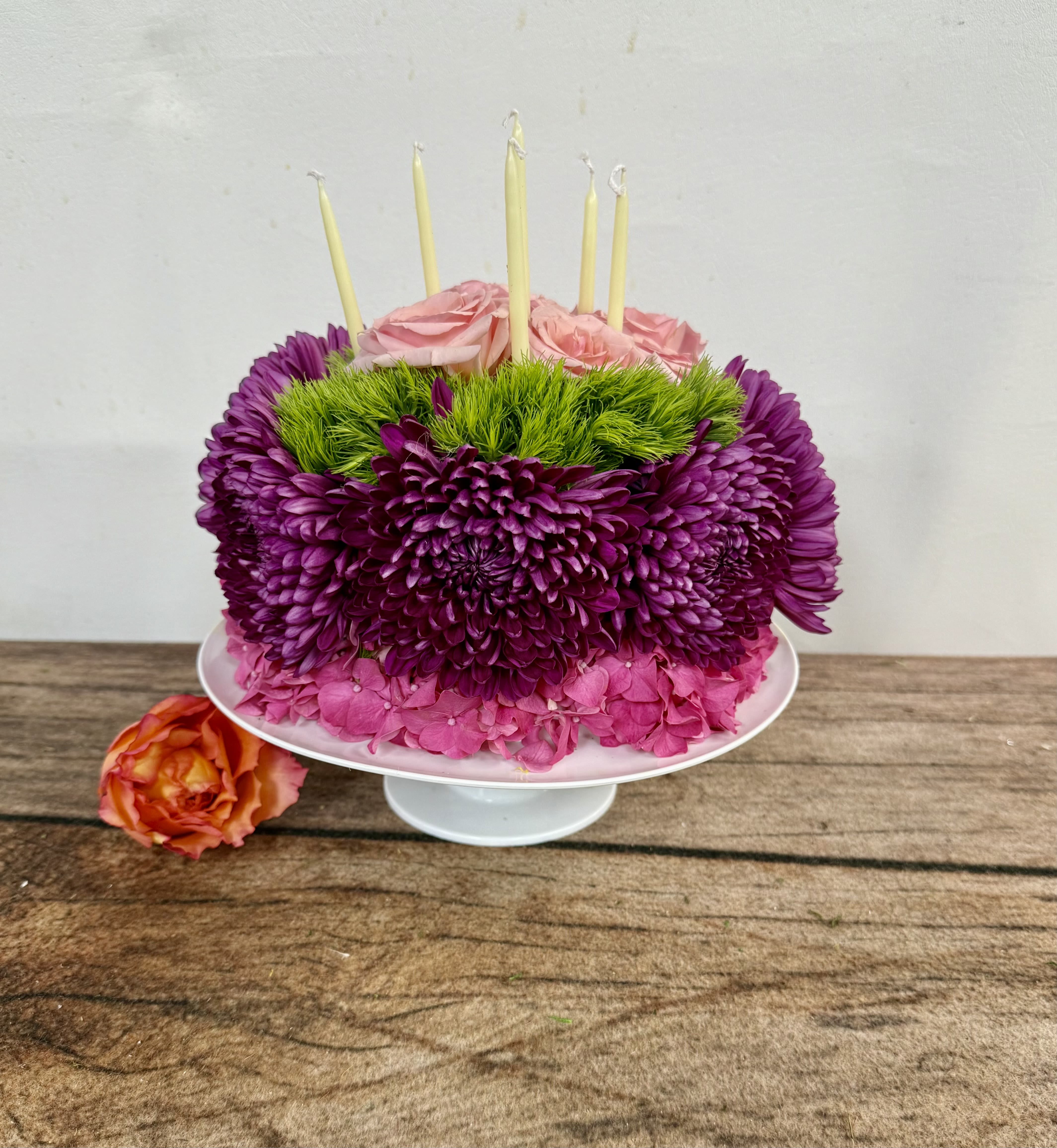 Pink and purple floral cake with candles on a white stand