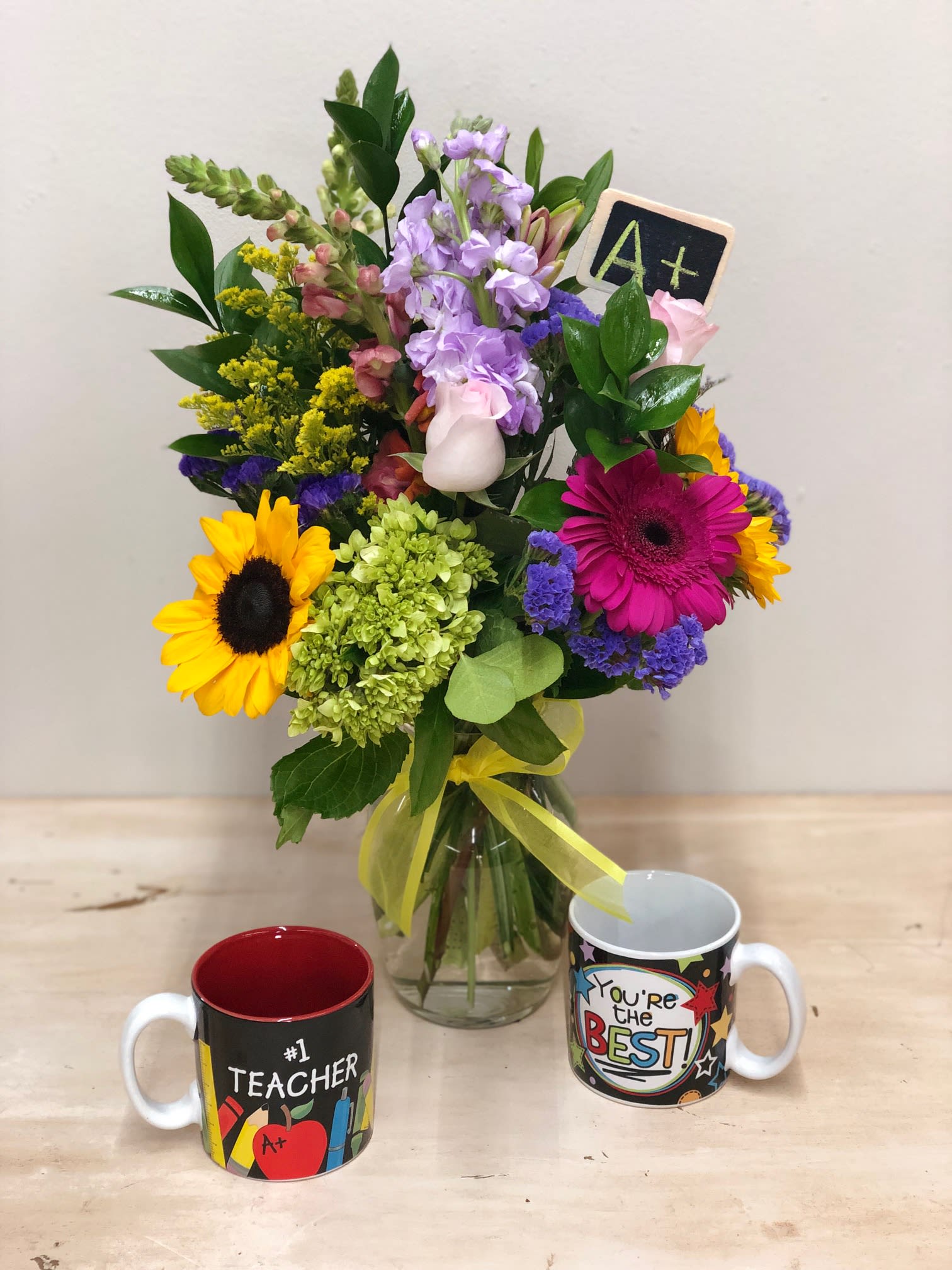 Mixed bouquet in a glass vase with two teacher-themed mugs in front