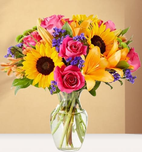 Bouquet of sunflowers, pink roses, and yellow lilies in a glass vase