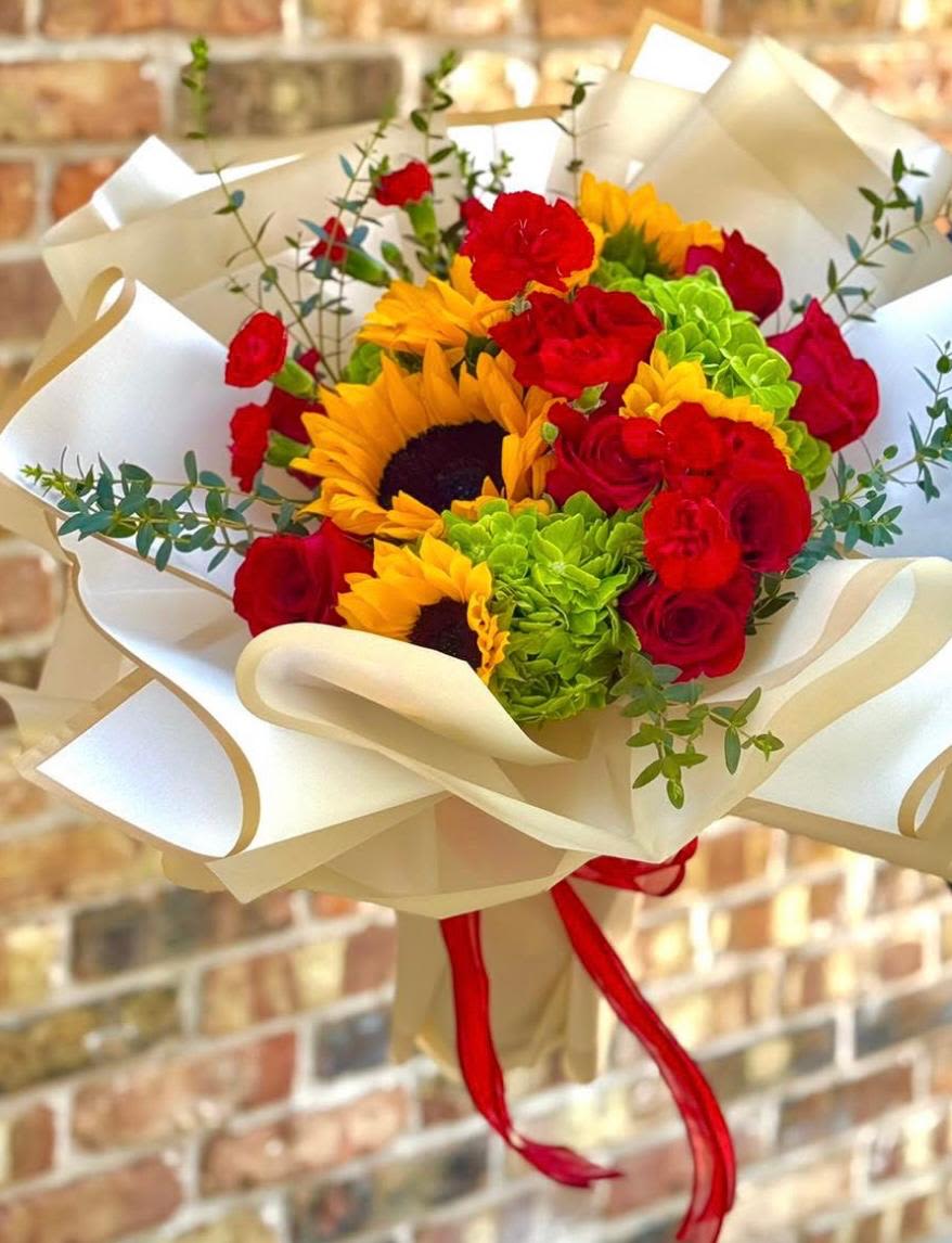 Bouquet of red roses, sunflowers, and green hydrangeas wrapped in cream paper