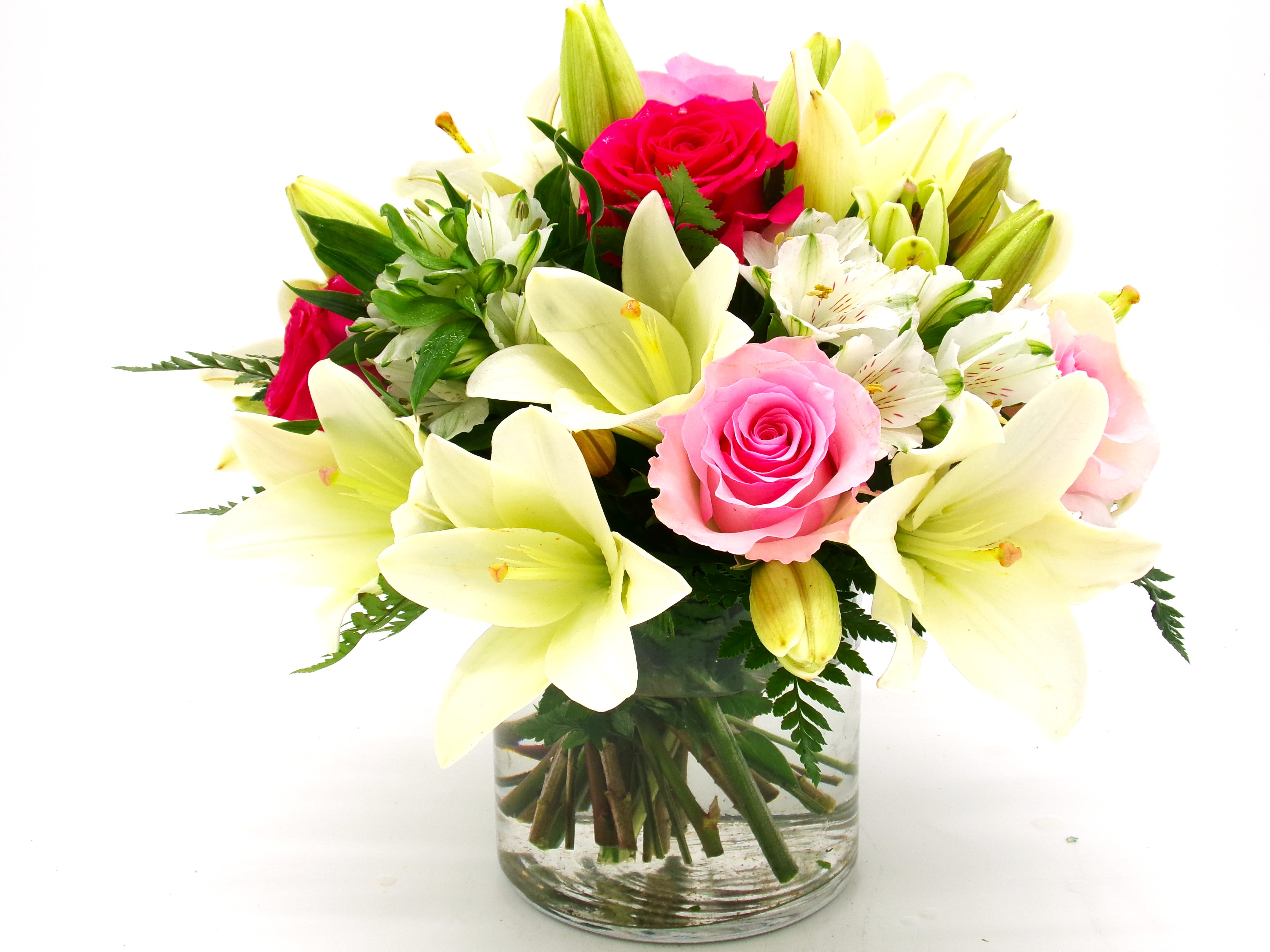 Candy Kiss - Large white lilies open like a soft halo around lively pink and red roses in this romantic flower arrangement for Mother's Day, anniversaries, birthdays, or to say "thank you." Candy Kiss is the kind of bouquet that makes the person you're thinking of feel cherished-fresh, fragrant lilies surround clusters of delicate white alstroemeria and rosy blooms for a look that reads both celebratory and intimate, perfect for love and romance or a thoughtful get-well wish.  This medium-sized, rounded arrangement is tightly gathered and presented in a clear glass vase that keeps the focus on the blooms. Pale cream lily petals frame brighter pink centers while red and pink roses add pops of color against the white alstroemeria and green foliage, giving a classic yet modern contrast. The compact, upright silhouette makes it easy to place on a bedside table, dining table, or office desk.  Send this bouquet when you want her to feel truly seen-whether marking an anniversary, saying happy birthday, or brightening recovery and everyday moments. Arrives ready-to-display in the included glass vase; trim stems and change the water every few days to help the lilies and roses stay fresh longer.