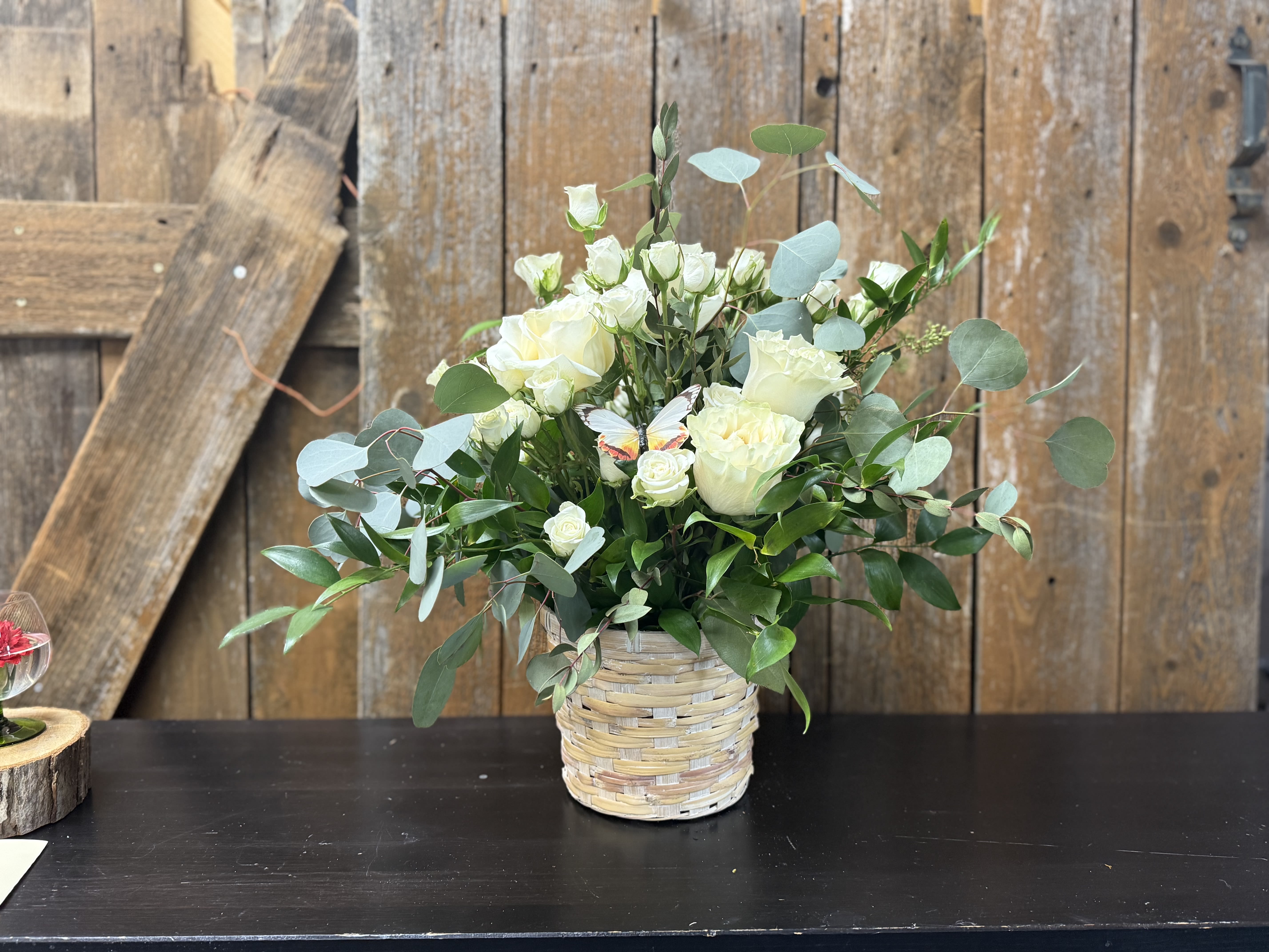 White roses in a woven basket vase with eucalyptus greenery