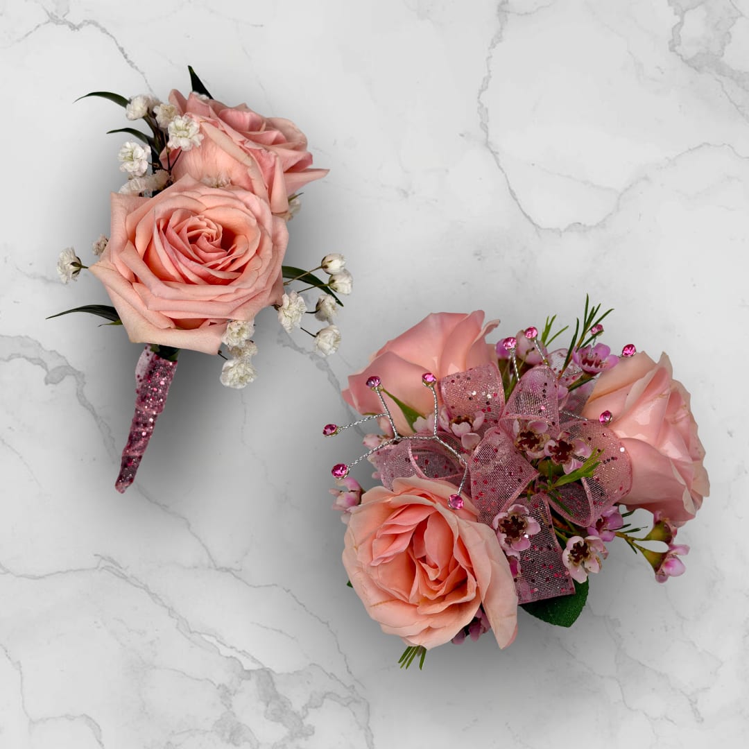 Rose Quartz 3 Rose Combo - Make ordering prom flowers a breeze this year with our Rose Quartz 3 Rose Combo! This combo comes with our Rose Quartz Boutonniere - With Wrap and our Rose Quartz 3 Rose Corsage, perfectly matched together to make a stunning, coordinating look.  The Rose Quartz 3 Rose Corsage is crafted with three blush pink spray roses and matching filler blooms in pink. This compact arrangement is finished with a sheer pink glitter ribbon threaded through the center for gentle shimmer. Pink decorative rhinestone gem picks with thin silver wire accents add subtle sparkle and formal polish, making the piece feel celebratory and refined.  The Rose Quartz Boutonniere - With Wrap features Two blush pink spray roses with baby's breath filler, wrapped in the shimmering pink sheer ribbon pictured, and a boutonniere pin is included so it sits neatly on a suit or jacket. 