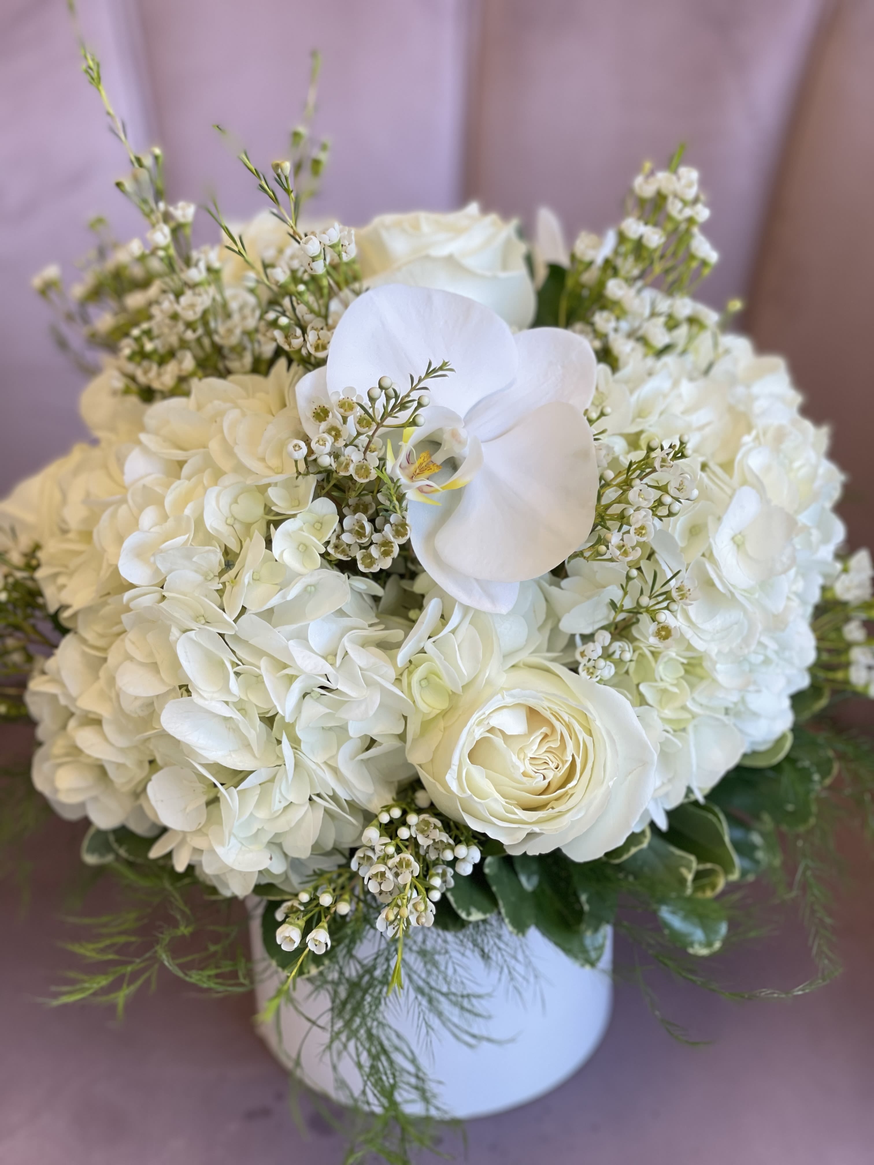 White floral arrangement in a round box with roses and hydrangeas