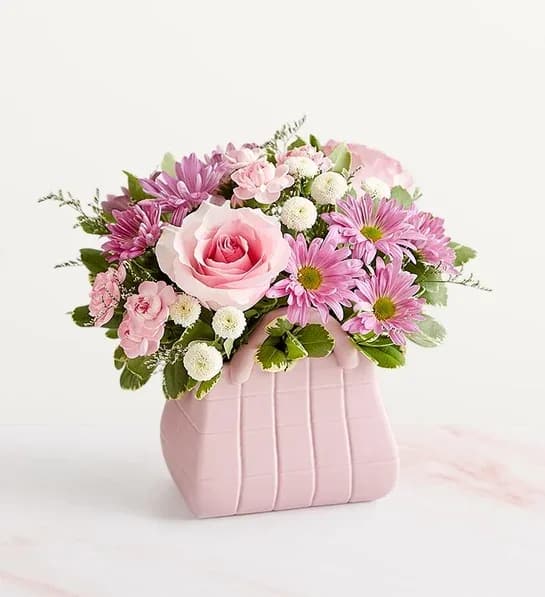Designer Dream - NEW The ultimate arrangement for your favorite fashionista. A profusion of roses, poms, and other blooms all but spill out of the top of our keepsake handbag-shape vase, making this a truly chic gift. And just like the perfect handbag, the pink, white, and lavender bouquet goes with just about everything.