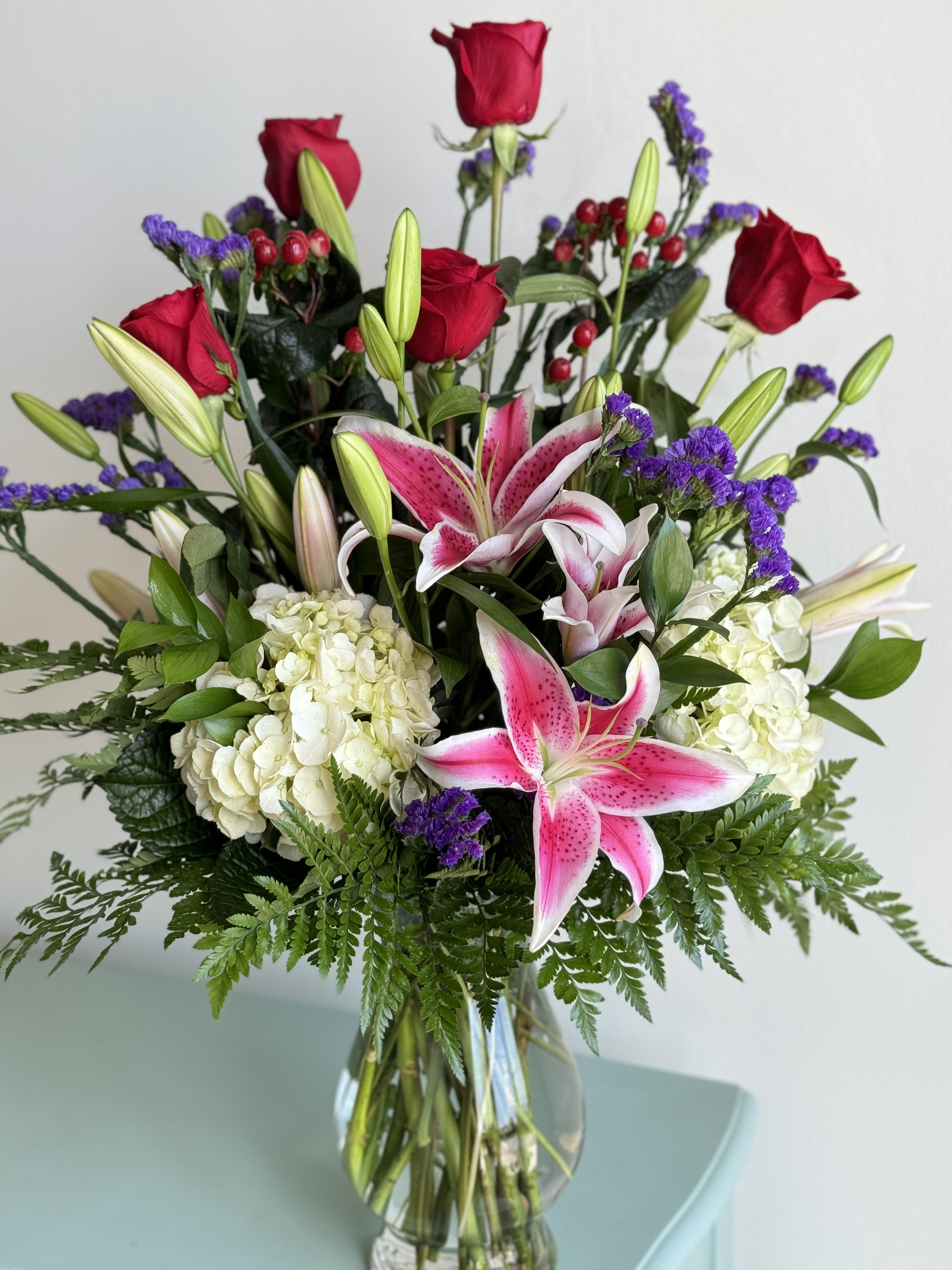 Bouquet of pink lilies, red roses, and white hydrangeas in a glass vase