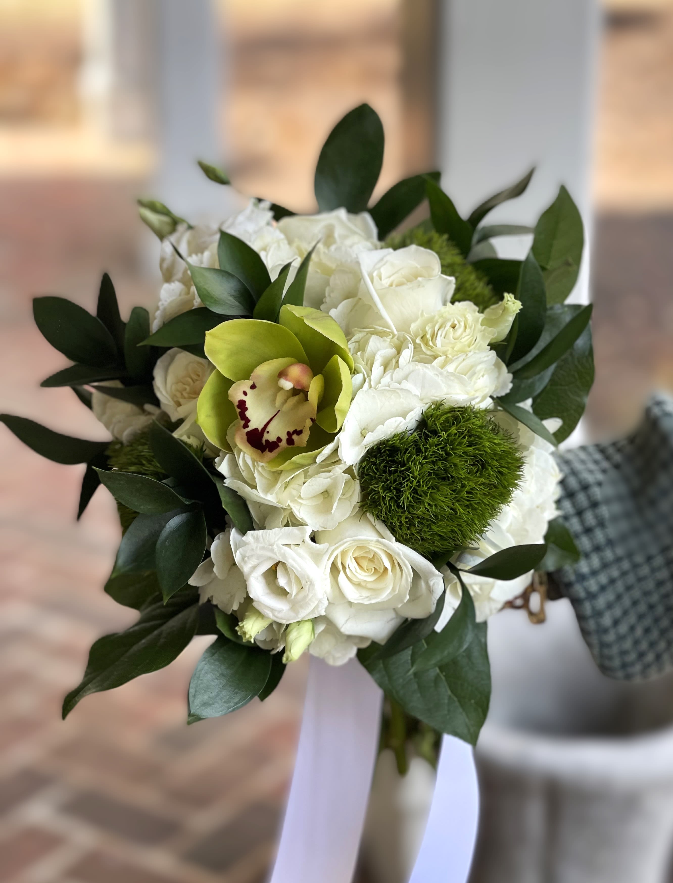 Hand-tied bouquet of white roses with green cymbidium orchid and mossy dianthus, finished with white ribbon tails