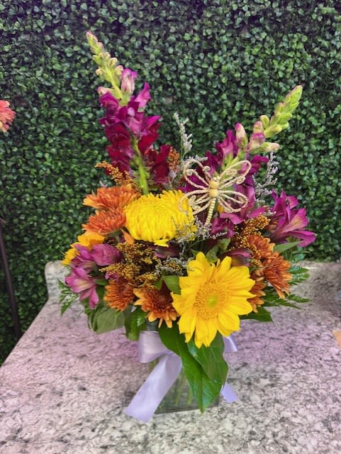 Colorful bouquet of yellow and orange flowers in a glass vase with a ribbon