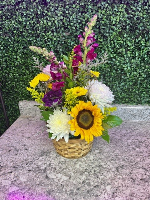 Mixed bouquet in a woven basket with sunflowers and white and purple blooms