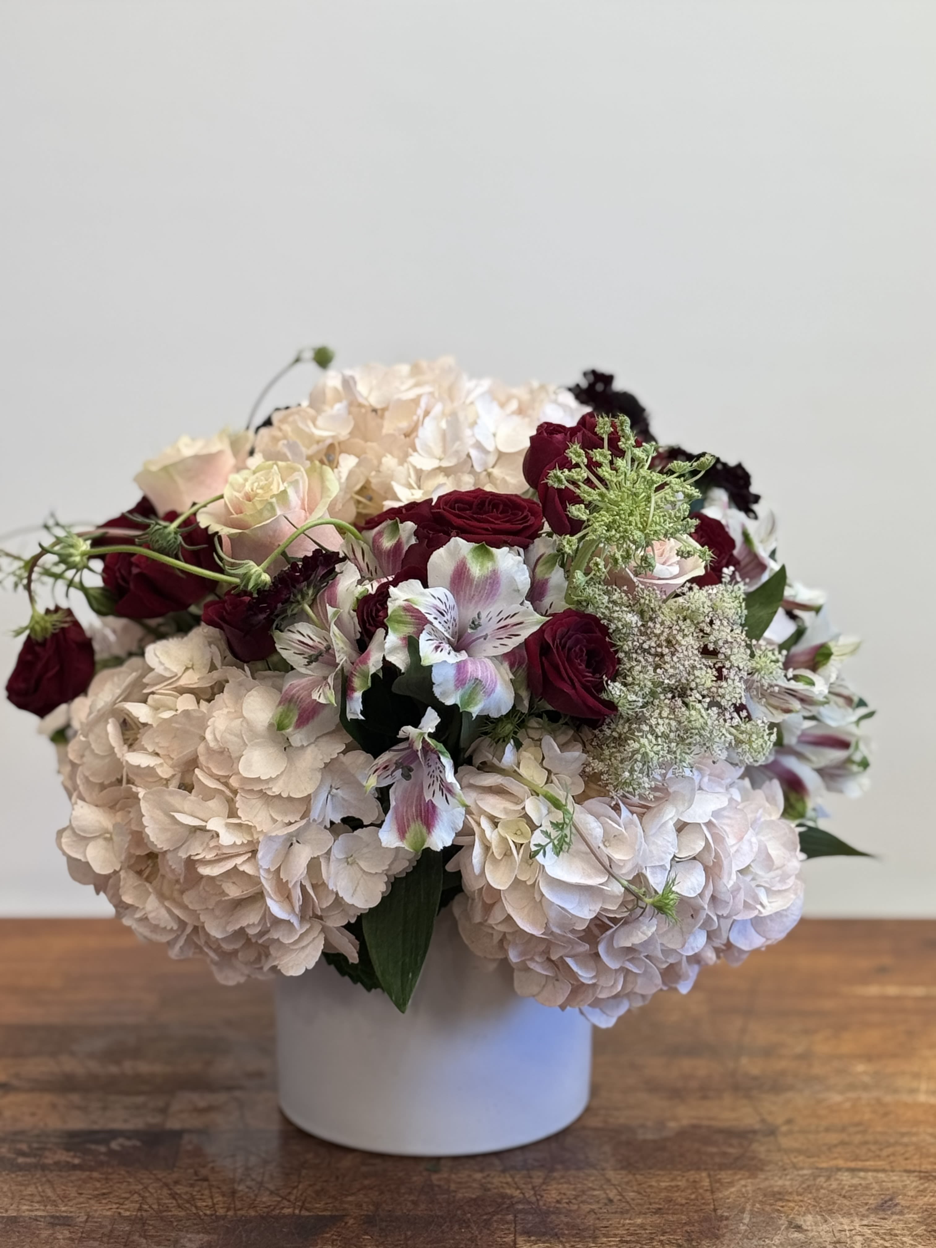 Bouquet of pale hydrangeas and burgundy roses in a white vase