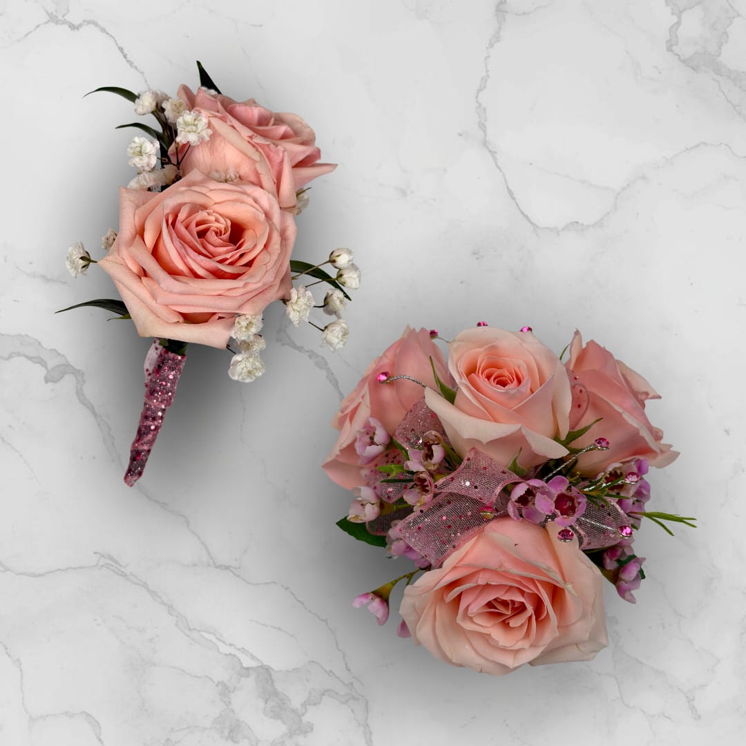 Rose Quartz 4 Rose Combo - Make ordering prom flowers a breeze this year with our Rose Quartz 4 Rose Combo! This combo comes with our Rose Quartz Boutonniere - With Wrap and our Rose Quartz 4 Rose Corsage, perfectly matched together to make a stunning, coordinating look.  The Rose Quartz 4 Rose Corsage is crafted with four blush pink spray roses and matching filler blooms in pink. This compact arrangement is finished with a sheer pink glitter ribbon threaded through the center for gentle shimmer. Pink decorative rhinestone gem picks with thin silver wire accents add subtle sparkle and formal polish, making the piece feel celebratory and refined.  The Rose Quartz Boutonniere - With Wrap features two blush pink spray roses with baby's breath filler, wrapped in the shimmering pink sheer ribbon pictured, and a boutonniere pin is included so it sits neatly on a suit or jacket. 