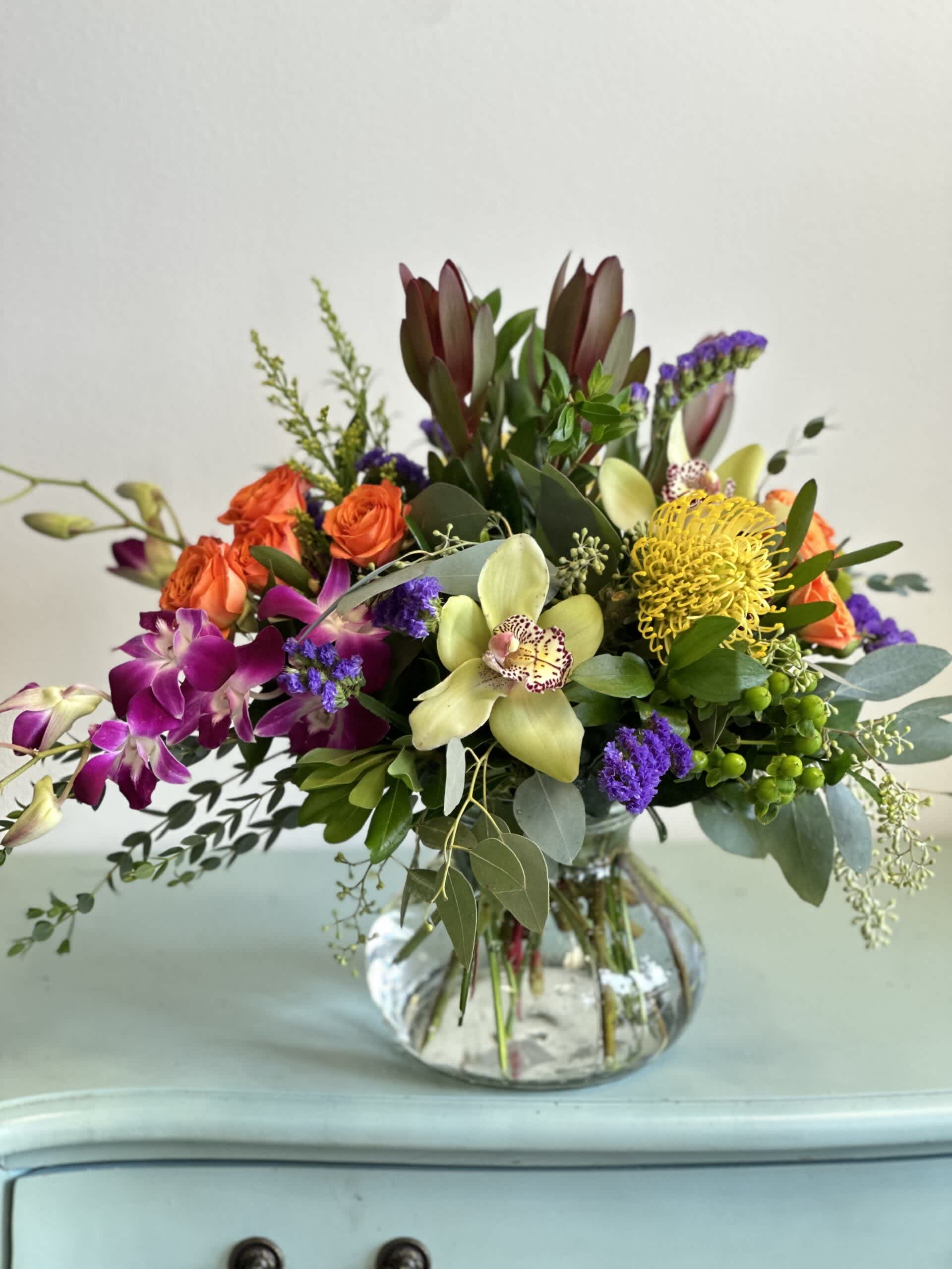 Mixed bouquet in a clear glass vase with orchids, roses, and yellow pincushion blooms