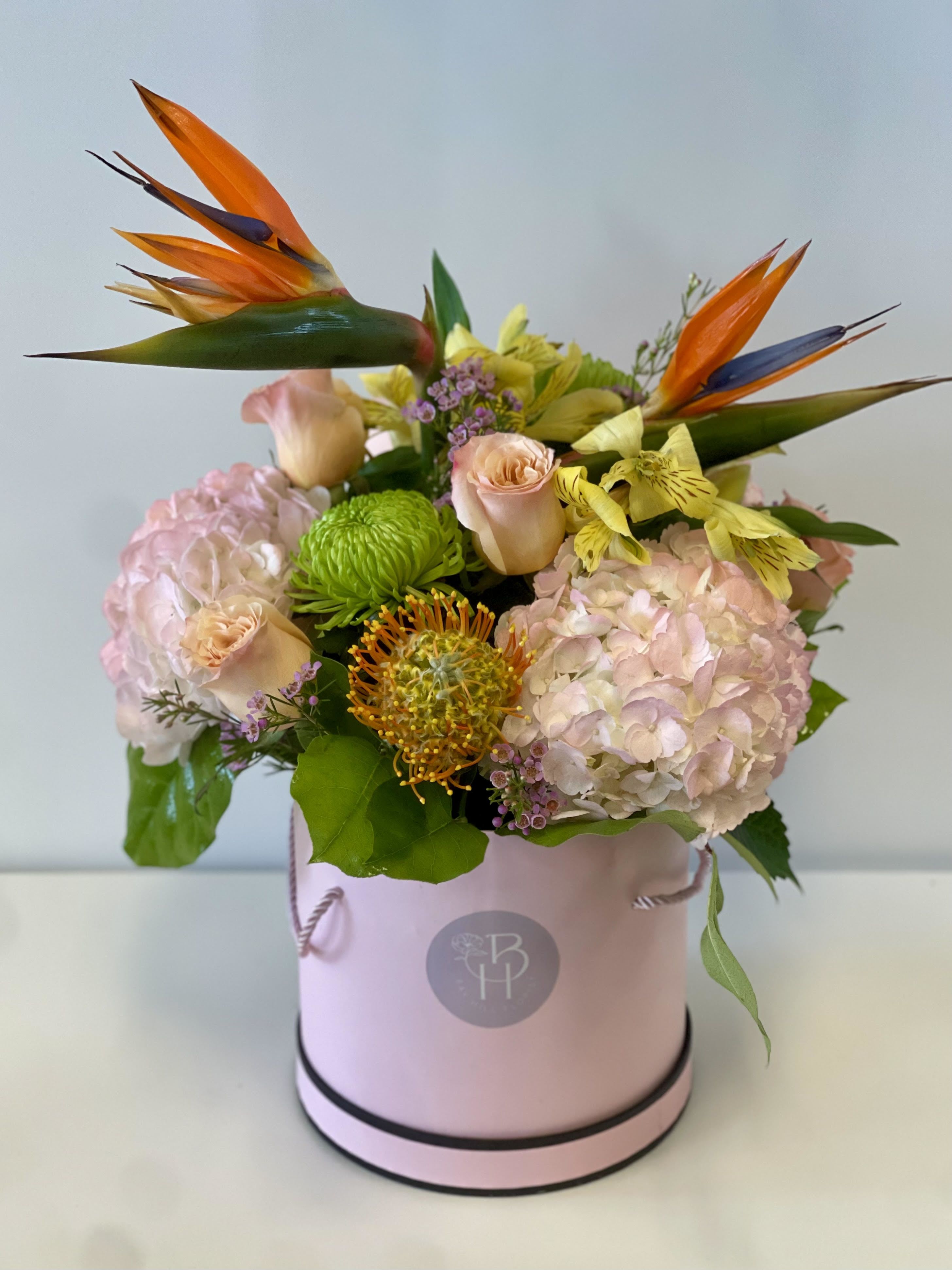 Pink floral arrangement in a round box with orange bird-of-paradise blooms