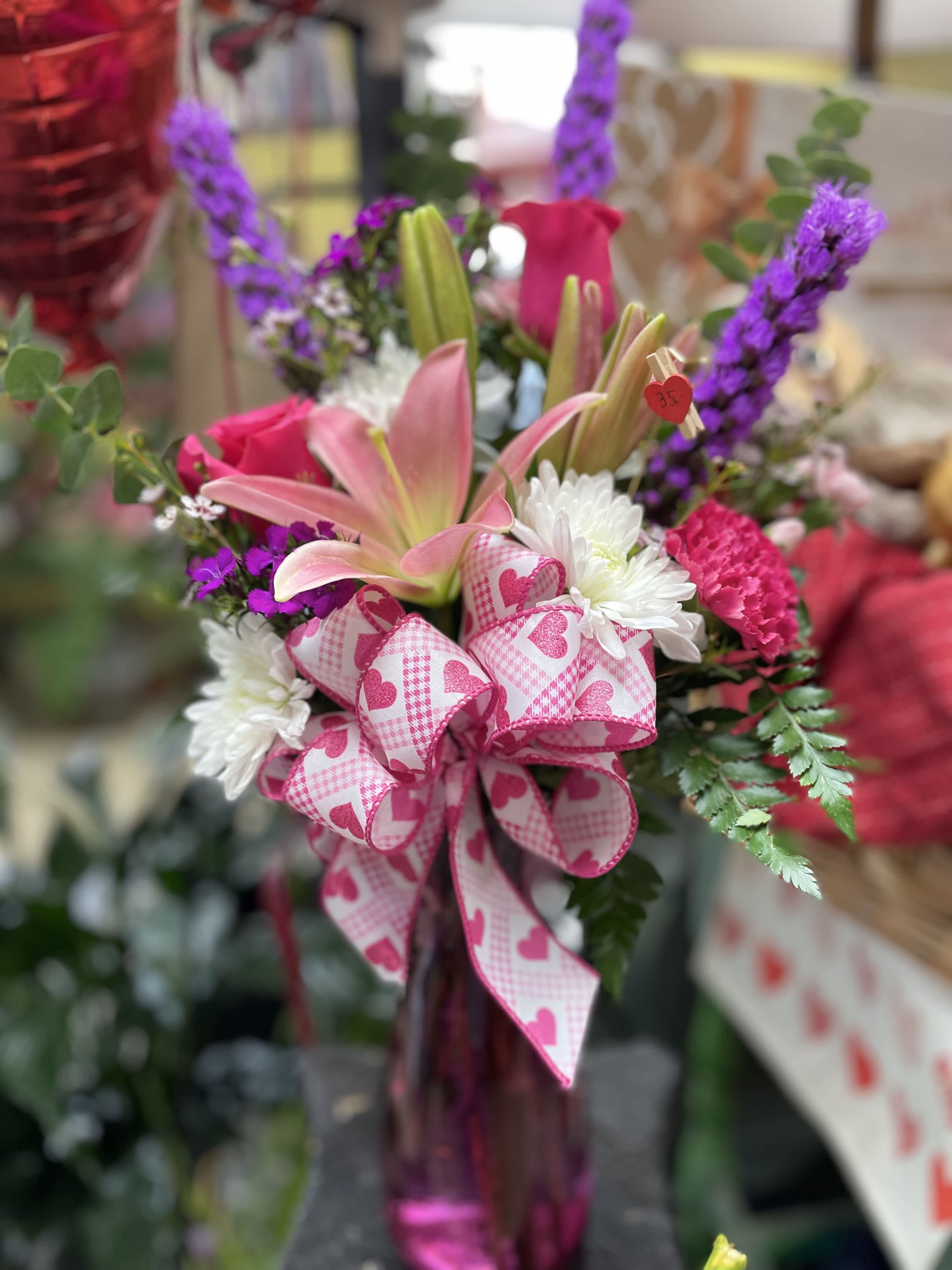 Pink lilies and roses with white daisies and a heart-patterned ribbon in a vase