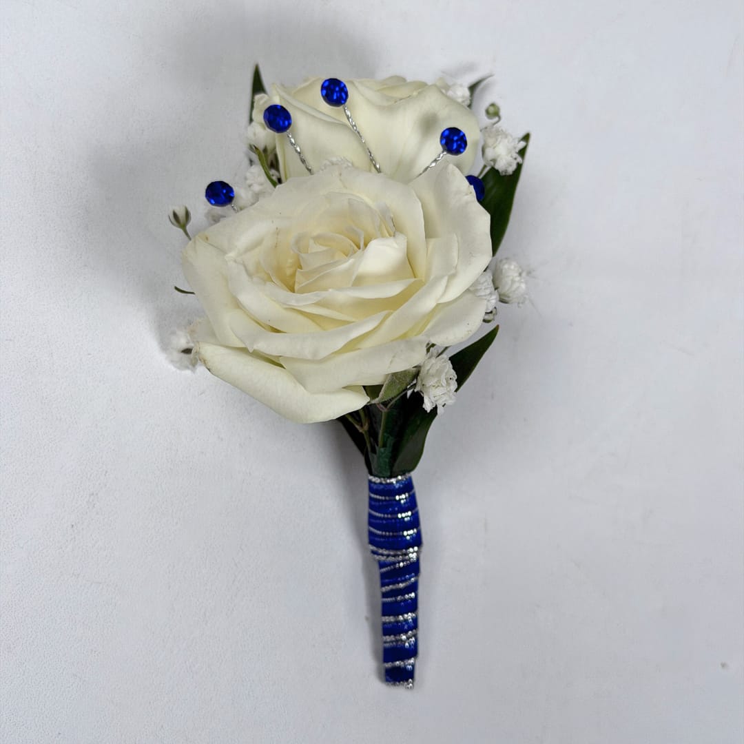 Sapphire Boutonniere - With Wrap and Sparkle - Two cream-white roses, clustered tightly with delicate white filler blooms and dark green leaves, create a quietly elegant boutonniere perfect for prom or other dressy occasions. The cool royal-blue and silver stem wrap gives this boutonniere a striking, refined accent, ideal for anyone who should stand out with subtle sophistication.  This version of the design is in the shimmering blue and silver ribbon pictured, and a boutonniere pin is included so it sits neatly on a suit or jacket. As an added final touch, this version also comes with a dazzling blue sparkle accent in your boutonniere, setting you apart from the rest with a subtle yet brilliant detail. If you want to change the color of either the ribbon wrap or add dazzling sparkle accents to your boutonniere, check out our add-ons and pick your desired color.