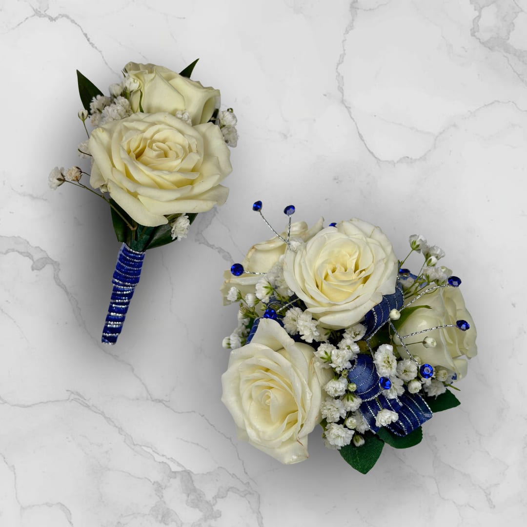 Sapphire 4 Rose Combo - Make ordering prom flowers a breeze this year with our Sapphire 4 Rose Combo! This combo comes with our Sapphire Boutonniere - With Wrap and our Sapphire 4 Rose Corsage, perfectly matched together to make a stunning, coordinating look.  The Sapphire 4 Rose Corsage features four cream-white roses that sit at the center, surrounded by clusters of tiny white filler blooms for soft texture. Wide blue ribbon loops provide a strong, elegant color pop while thin silver wire picks topped with bright blue gem-like rhinestones add sparkle and structure. The rounded, compact composition is small and wearable with an attached white lace wristlet, designed to complement dresses and suits without overwhelming the outfit.  The Sapphire Boutonniere - With Wrap features two cream-white roses, clustered tightly with delicate white filler blooms and dark green leaves. The cool royal-blue and silver stem wrap gives this boutonniere a striking, refined accent, ideal for anyone who should stand out with subtle sophistication.