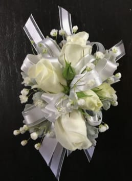 White Wrist Corsage - Creamy white roses arranged in a compact, rounded cluster give this white wrist corsage an elegant, timeless look perfect for a wedding or prom. The soft palette of whites and mixed neutral tones reads as quietly refined, so the person you're celebrating will feel composed and polished-exactly right for a bride, bridesmaid, or someone stepping out for a formal evening.  Small white filler blooms surround the roses for delicate texture, while wide silver satin ribbon is woven through the design and tied to form the wrist band, adding a polished, formal finish. The corsage sits close to the wrist in a hand-held scale that complements gown sleeves and tuxedo accents; its restrained colors keep it versatile across seasons and styles.  For a wedding party or prom date, this corsage says classic, understated elegance-an effortless way to make the recipient feel cherished. Care is simple: keep it cool and mist lightly if needed, and request same-day local delivery or specify timing so it arrives fresh for the event.