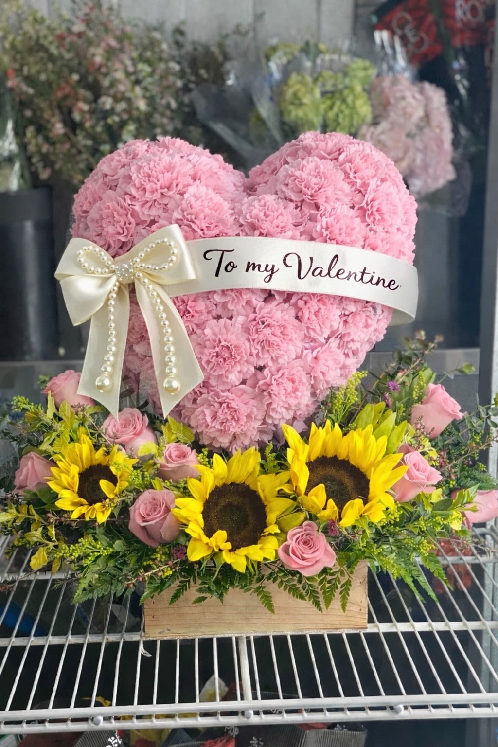 Pink heart-shaped floral arrangement with a Valentine ribbon and sunflowers below