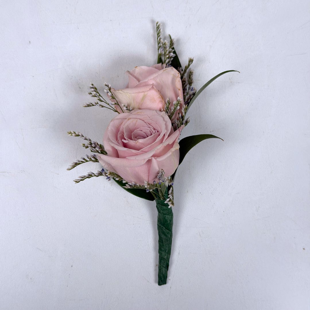 Amethyst Boutonniere - Soft pale lavender roses take center stage in this Amethyst boutonniere, a romantic boutonniere perfect for weddings, proms, or anniversary wear. The two lavender spray roses are paired with tiny white and lavender filler sprigs and slender dark green leaves, creating a compact, diagonal composition with gentle texture and movement. The overall palette of lavender, white and green keeps the look soft and versatile.  The standard design is hand-wrapped with dark green stem wrap and a boutonniere pin is included so it sits neatly on a suit or jacket. Upgrade to deluxe to have your boutonniere wrapped in the shimmering iridescent ribbon pictured. Upgrading to premium includes this ribbon wrap, and also adds iridescent rhinestone sparkle accents to introduce a delicate extra shine for dressy occasions.  If you want to change the color of either the ribbon wrap or the sparkle accents, check out our add-ons and pick your desired color.