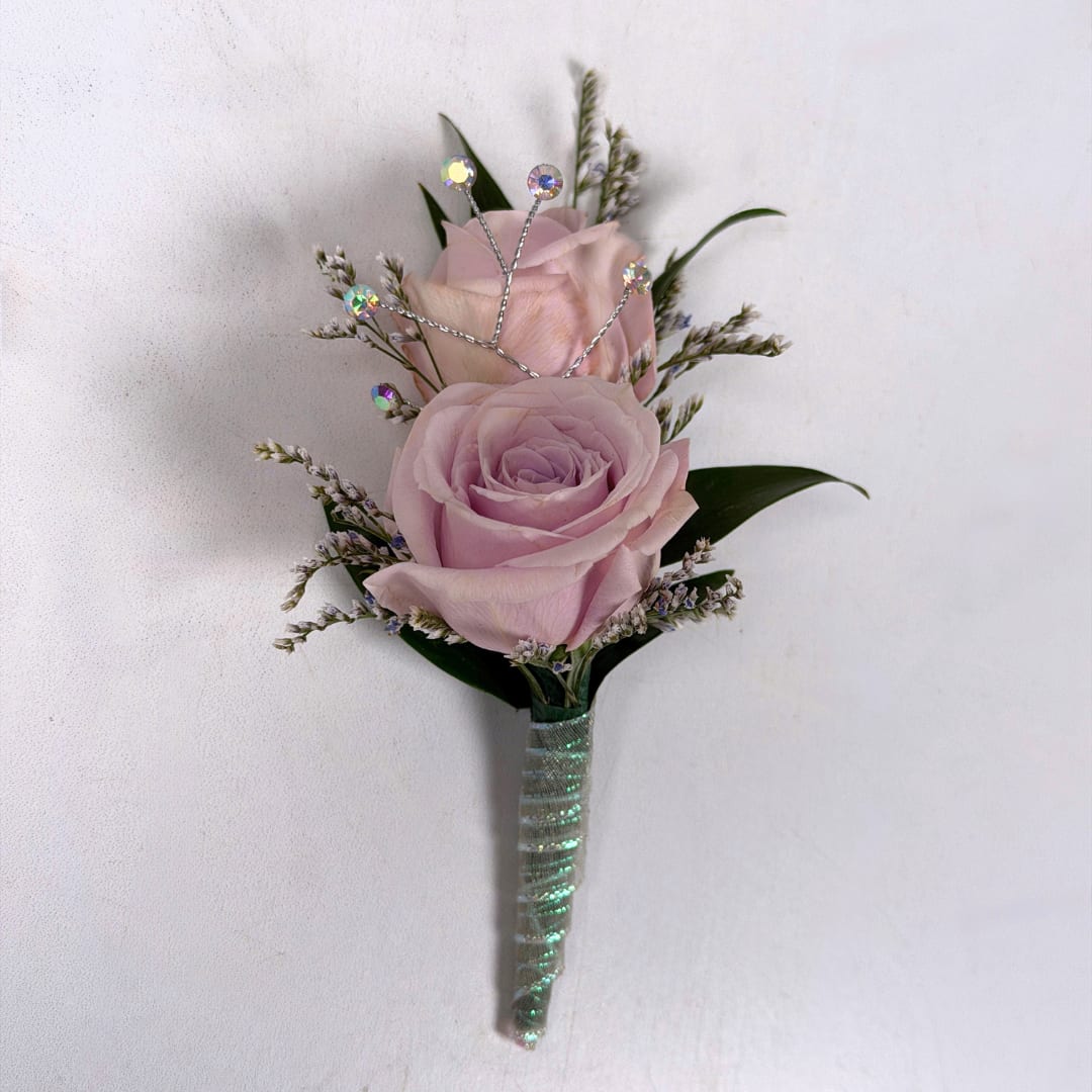 Amethyst Boutonniere - With Wrap and Sparkle - Soft pale lavender roses take center stage in this Amethyst boutonniere, a romantic boutonniere perfect for weddings, proms, or anniversary wear. The two lavender spray roses are paired with tiny white and lavender filler sprigs and slender dark green leaves, creating a compact, diagonal composition with gentle texture and movement. The overall palette of lavender, white and green keeps the look soft and versatile.  This version of this design is the most spectacular of them all, with a shimmering iridescent ribbon wrap creating a subtle shine to this boutonniere, and a stem of iridescent rhinestone sparkle accents is the final dazzling touch to make your night even more special. A boutonniere pin is included so it sits neatly on a suit or jacket without any fuss so you can spend your evening dancing the night away.  If you want to change the color of either the ribbon wrap or the sparkle accents, check out our add-ons below or at checkout and pick your desired color.