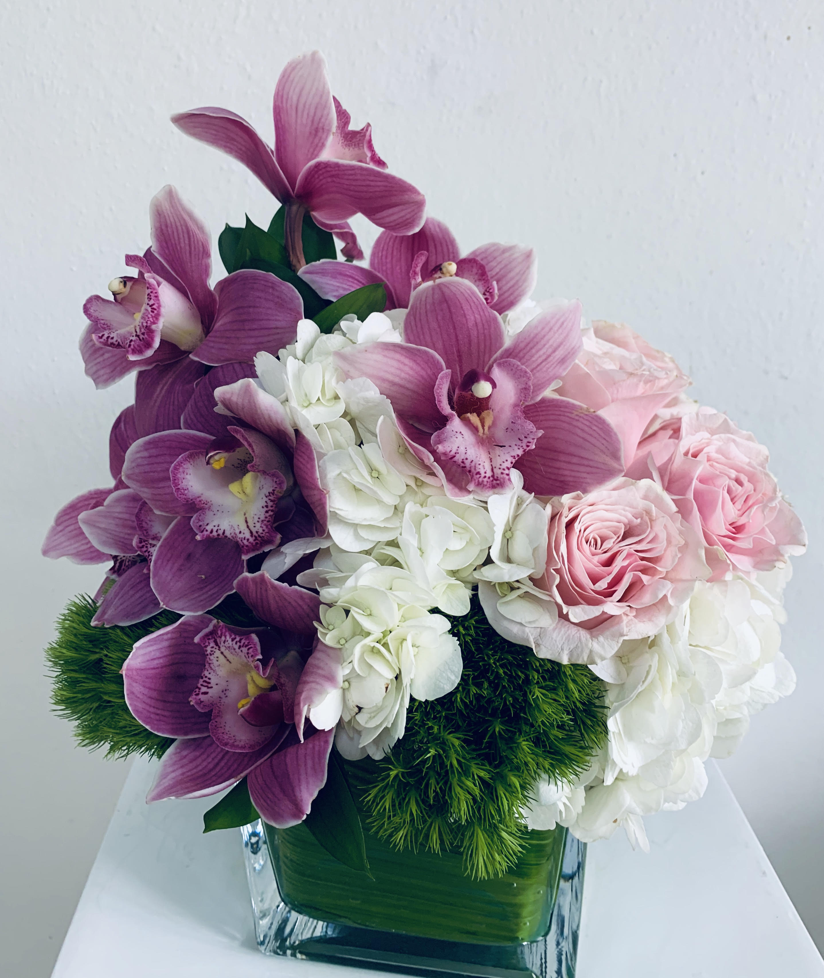 Pink orchids and roses arranged in a square glass vase