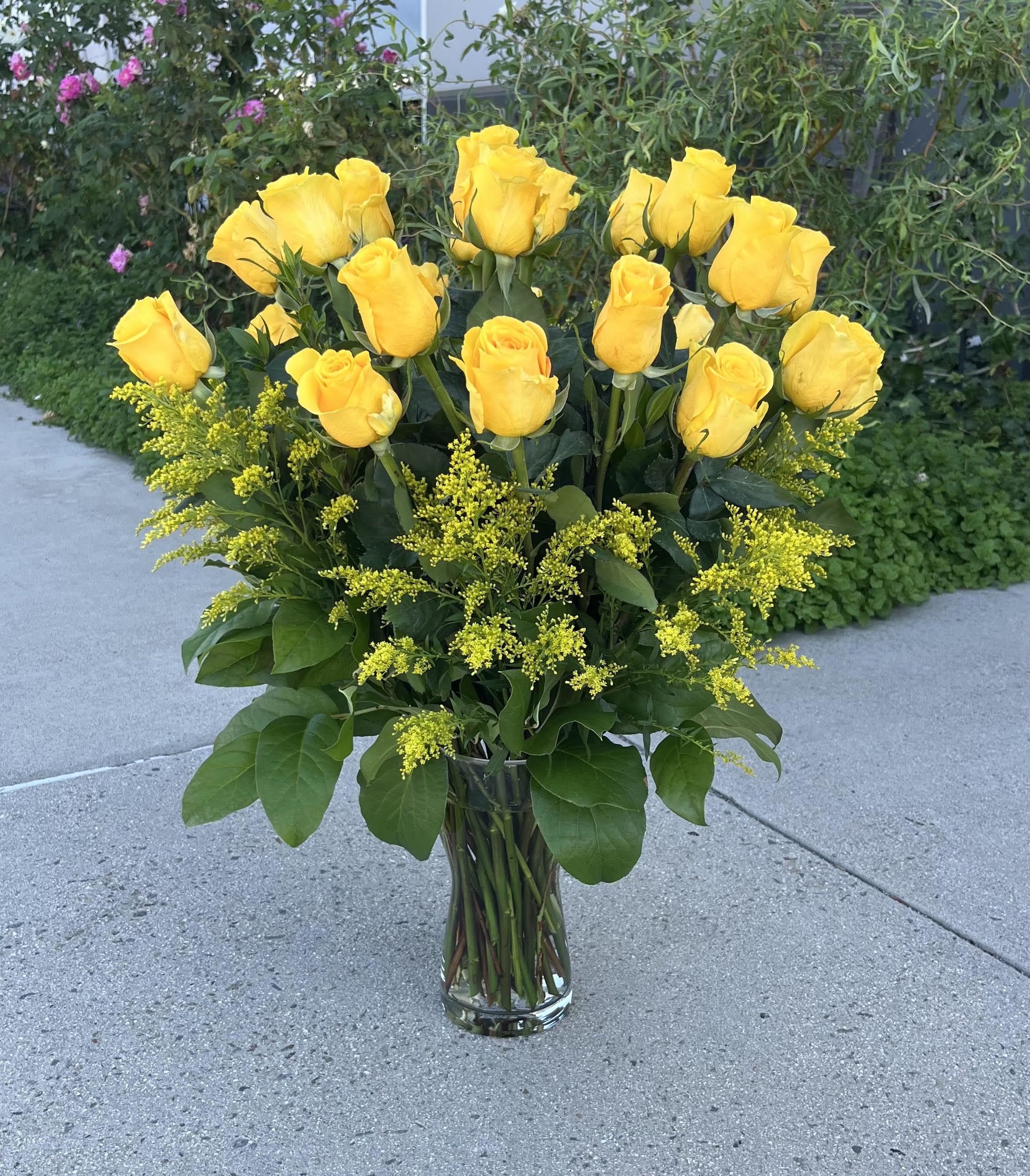 Yellow roses arranged in a clear glass vase with yellow filler flowers