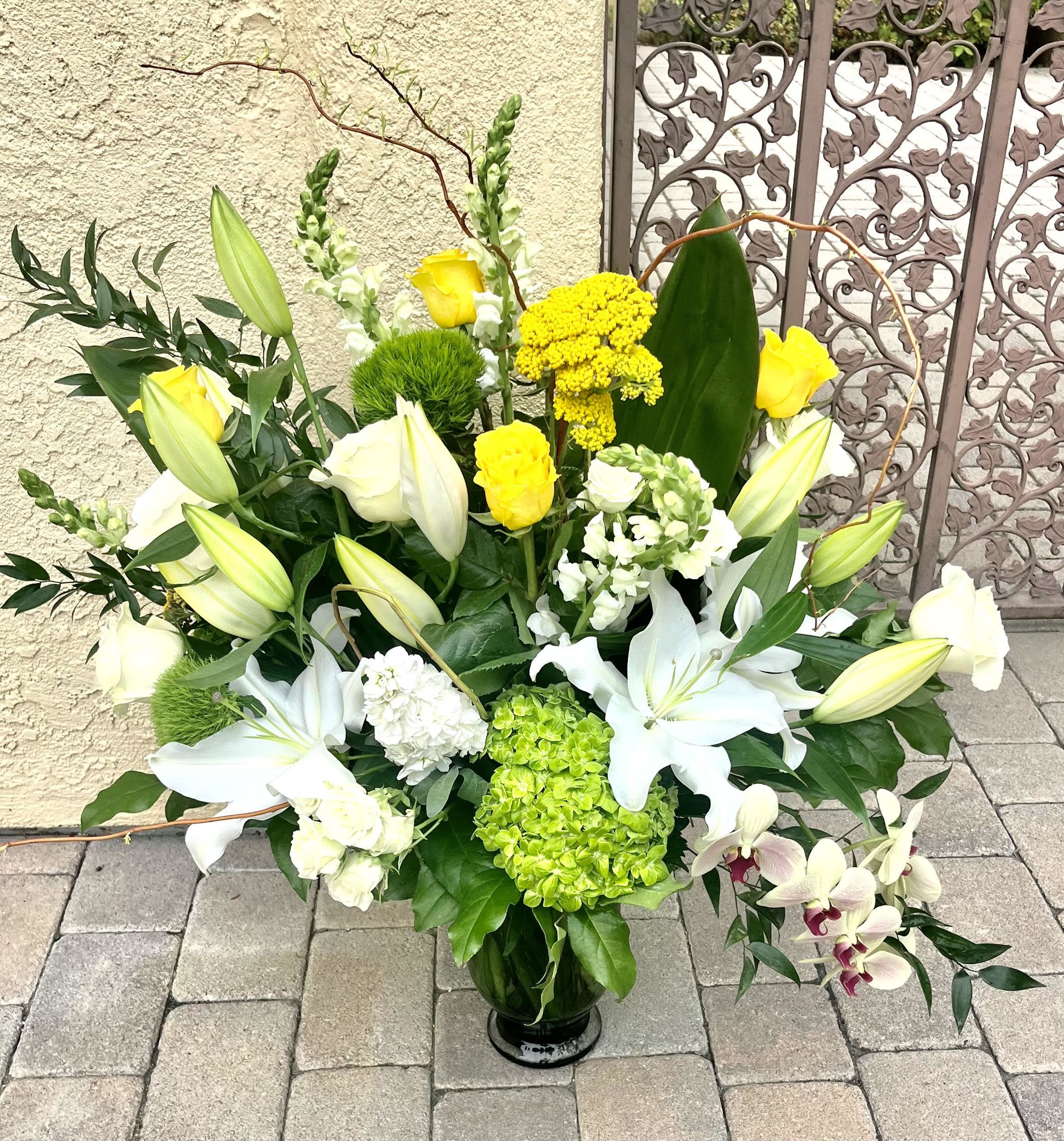 Large floral arrangement with white lilies, yellow roses, and green hydrangea in a vase