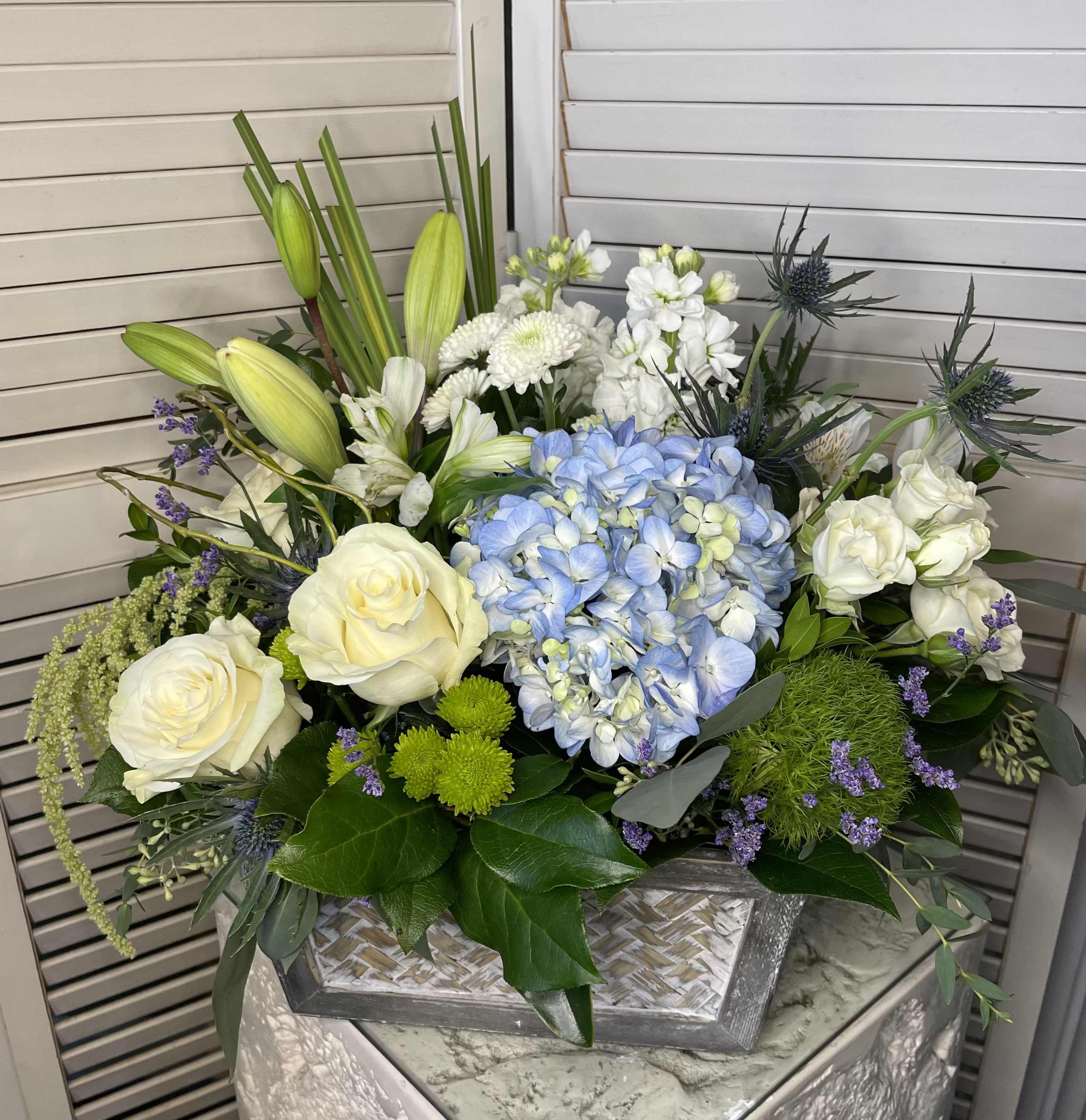 Mixed floral arrangement with white roses, blue hydrangea, and lilies in a silver container