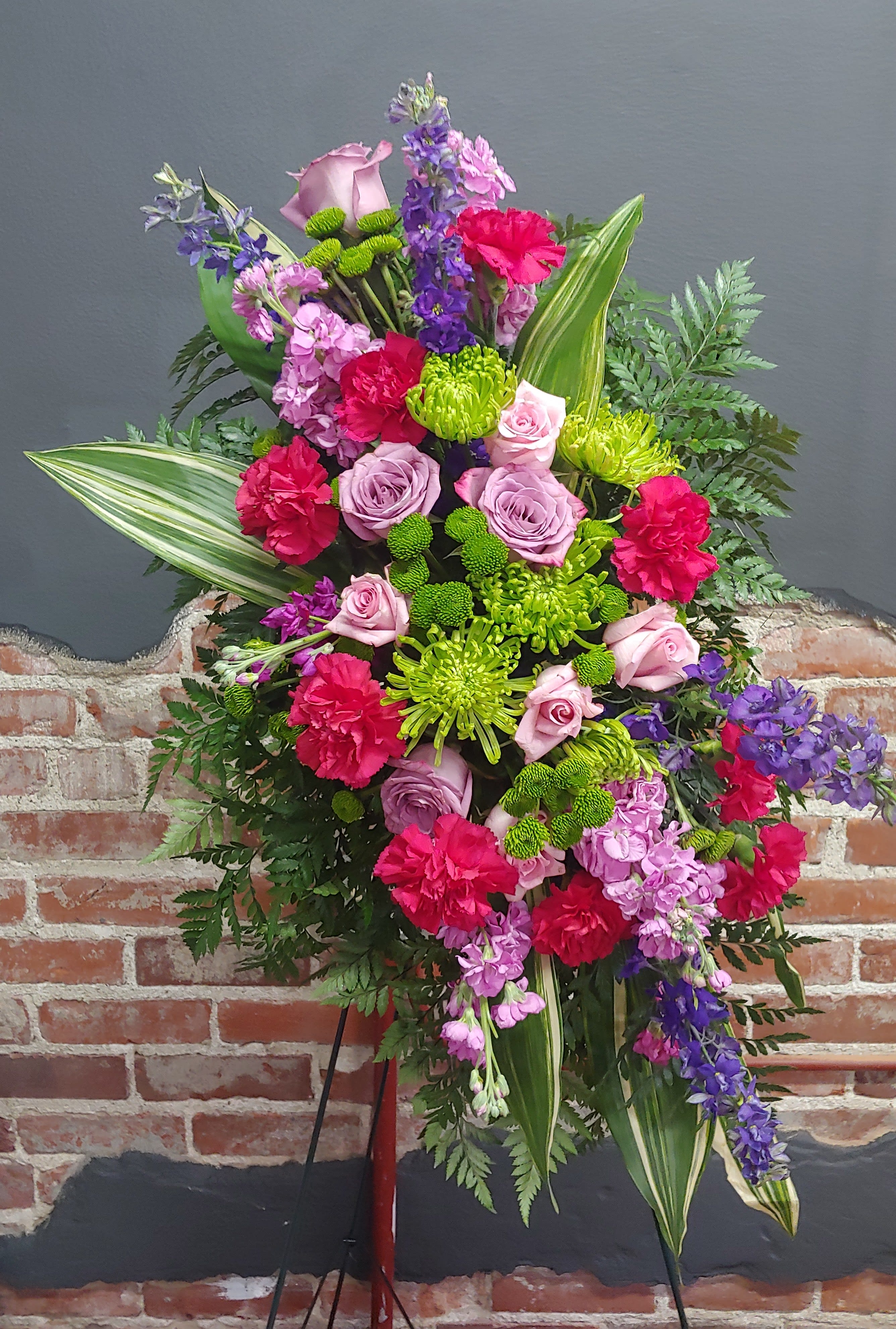 Standing floral spray with pink roses, carnations, and purple blooms