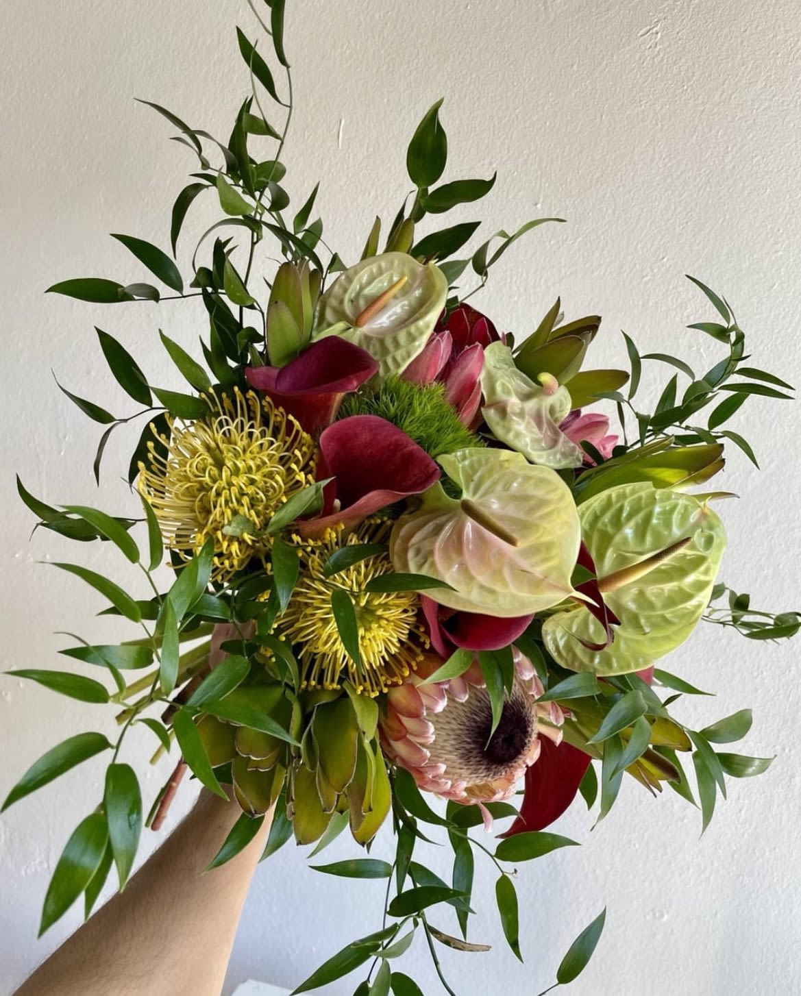 Tropical bouquet with red anthuriums, yellow pincushion blooms, and greenery