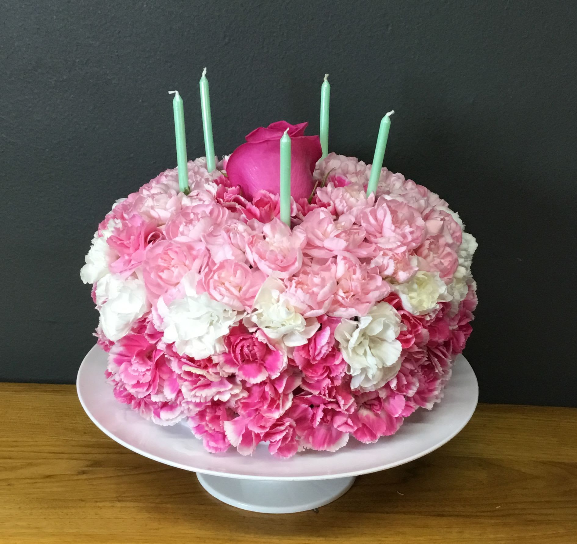Pink and white floral cake with mint green candles on a pedestal stand