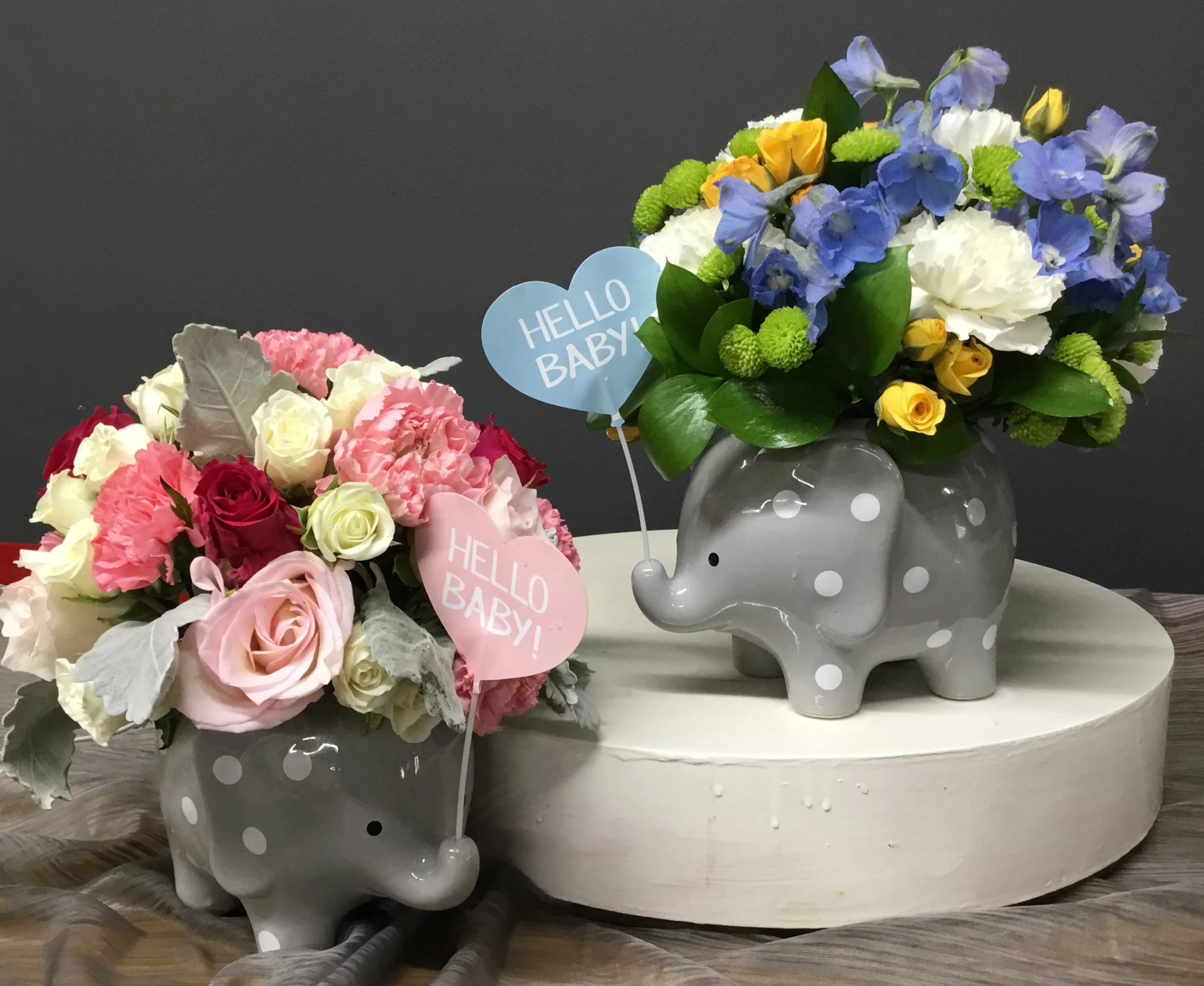 Two polka dot elephant vases filled with mixed pastel flowers and Hello Baby heart picks.