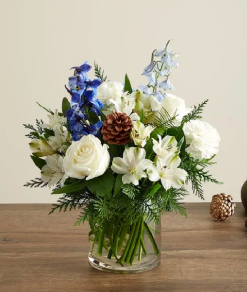 Winter Wishes - Inspired by winter’s cool blue &amp; white landscape, our delightful arrangement delivers warm wishes to the people you love. Hand-designed with a lush gathering of blooms, evergreens and rustic touches, it’s a thoughtful sentiment filled with the season’s natural beauty.